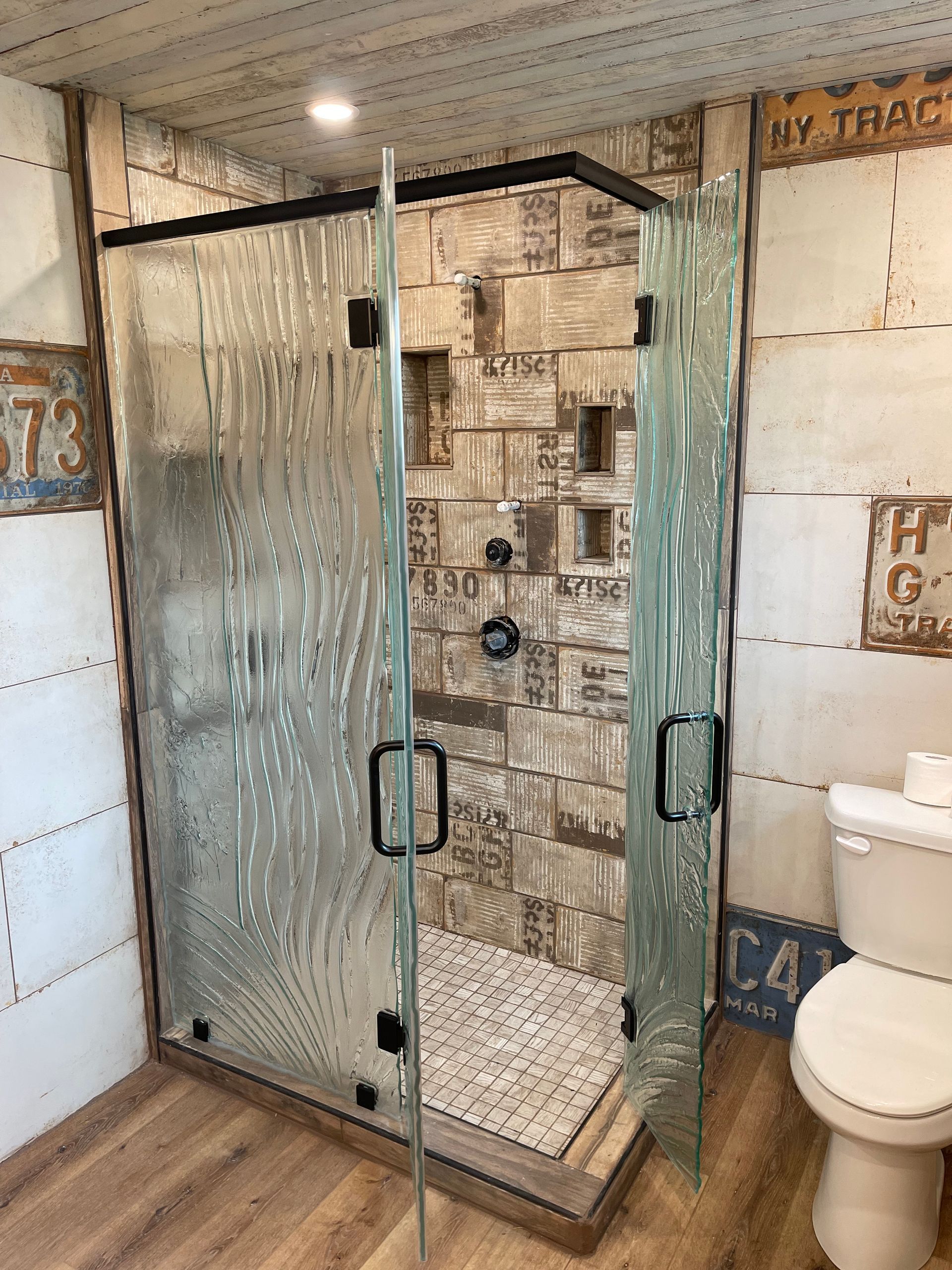 Shower with textured glass doors and license plate-themed tile, next to a toilet.