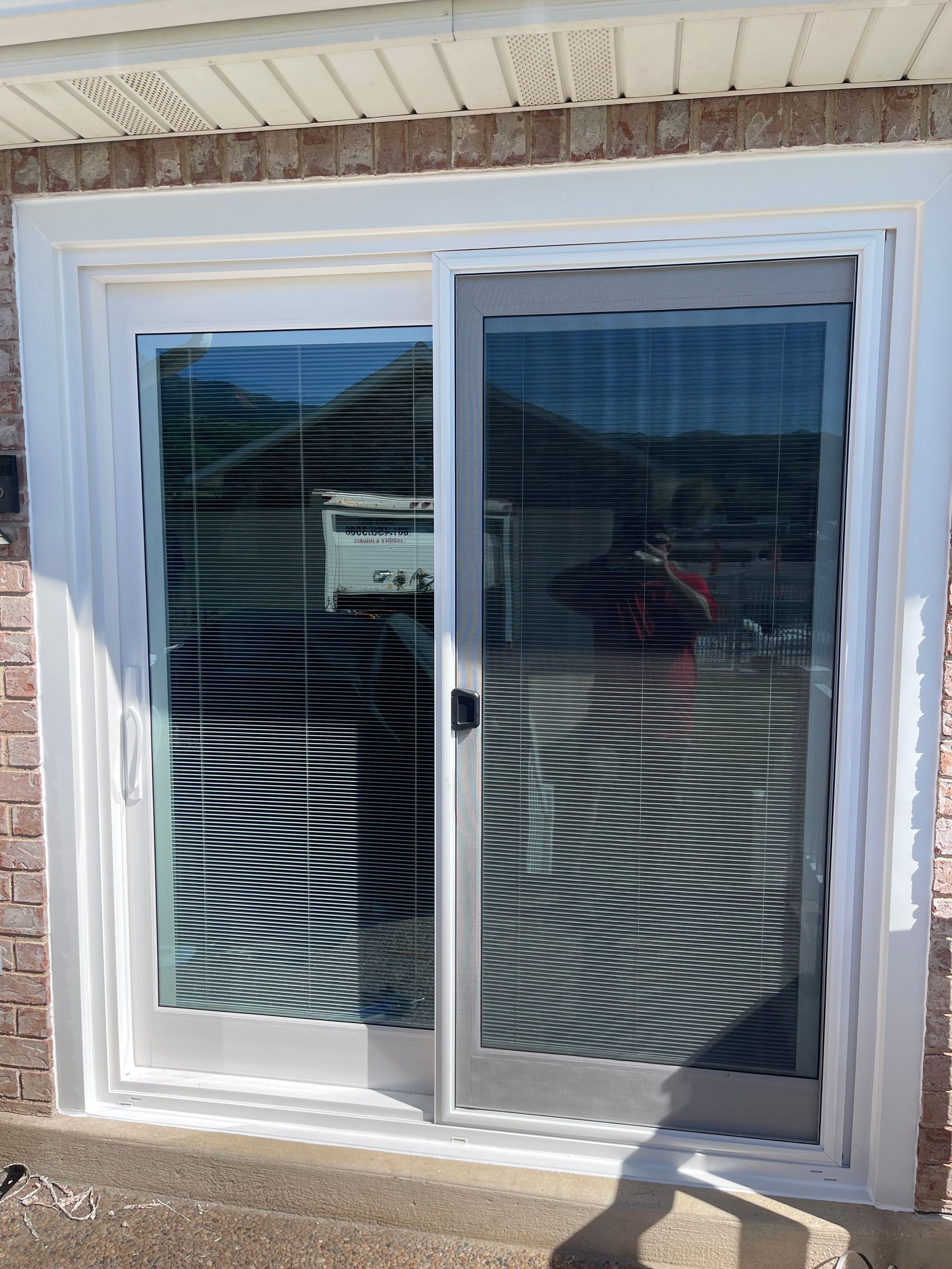 Sliding glass door with white frame, reflecting trees and house with brick siding.