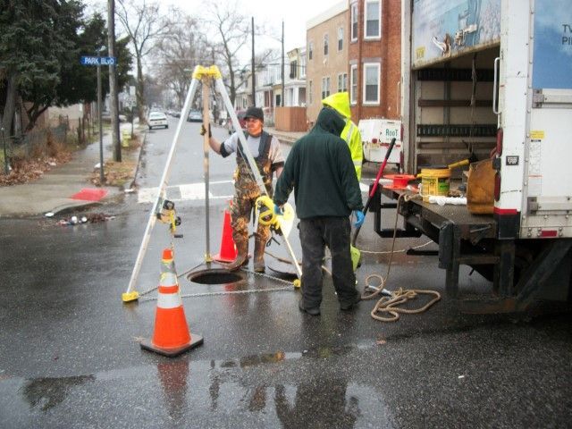 A group of men are working on a manhole on the side of the road
