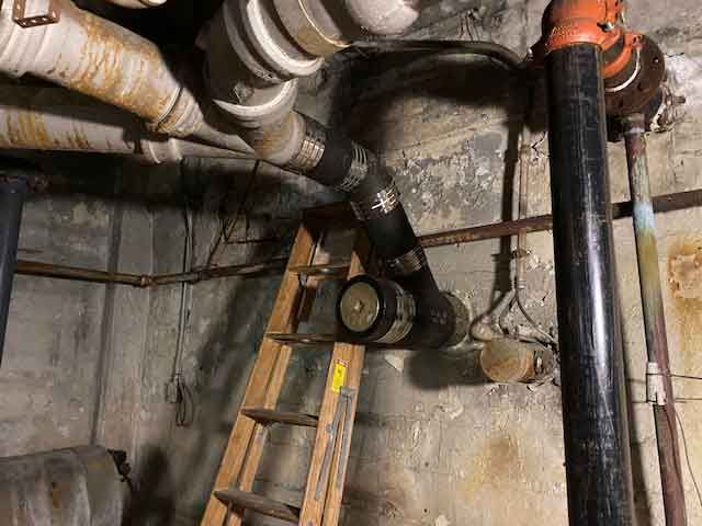 A ladder is sitting next to a bunch of pipes in a basement.