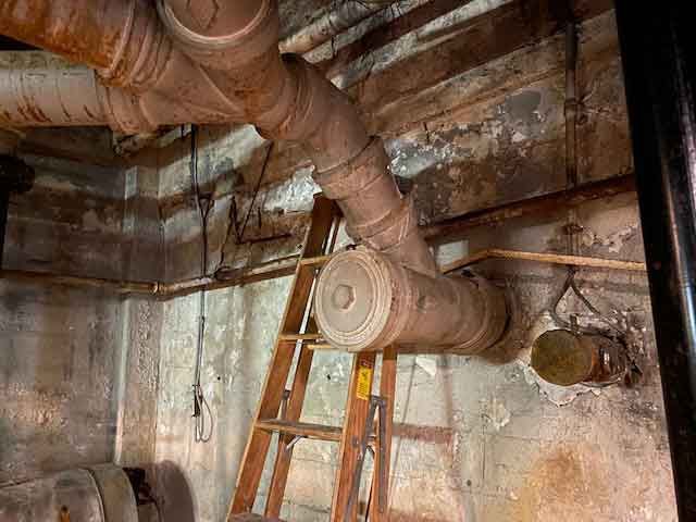 A ladder is sitting next to a bunch of pipes in a room.