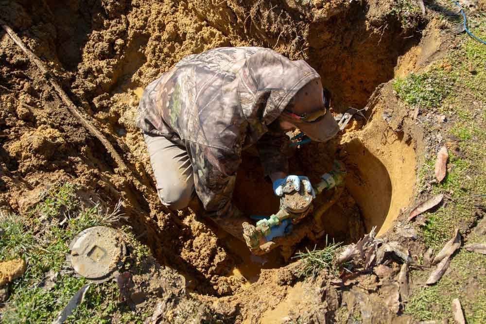 A man is digging a hole in the dirt with a shovel.