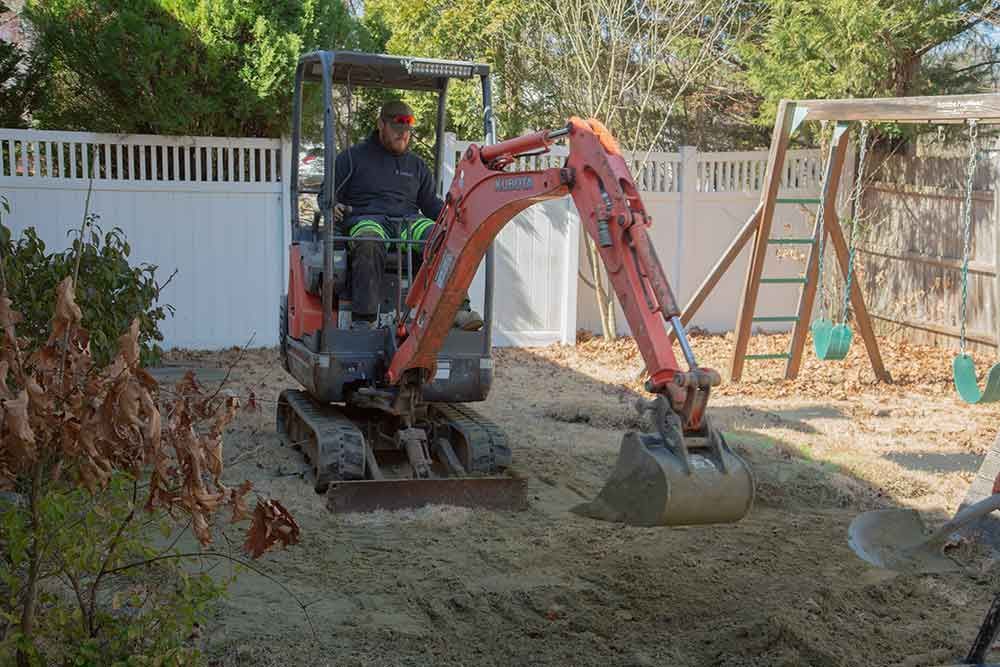 A man is driving a small excavator in a backyard.