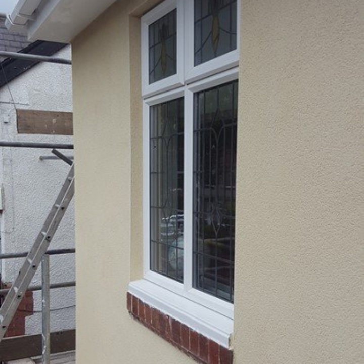 Cream-colored stucco exterior with white window frame, red brick trim, and a ladder against the adjacent wall.