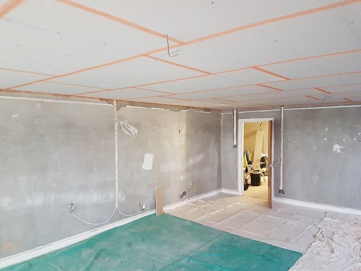 Room under renovation: gray walls, white ceiling, door frame, exposed wires, green floor covering.