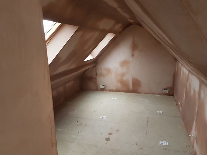 Interior of a renovated attic room with slanted walls, skylights, and fresh plaster.