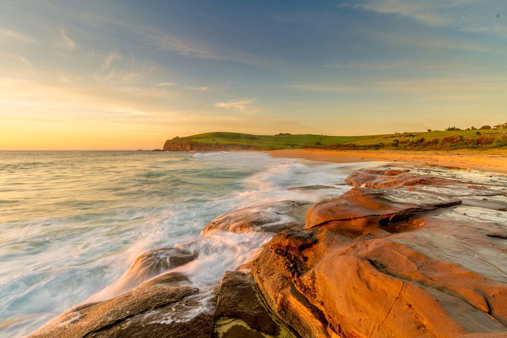 A Sunset Over A Rocky Beach With Waves Crashing Against The Rocks — B Smart Building & Design In Gerringong, NSW
