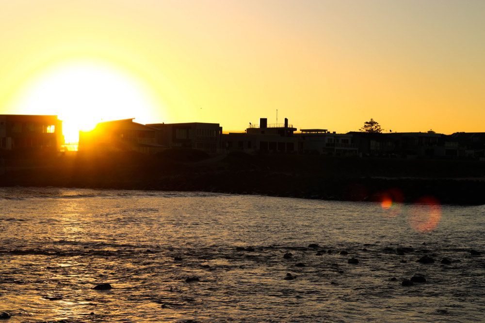The Sun Is Setting Over A Body Of Water With Buildings In The Background — B Smart Building & Design In Shellharbour, NSW