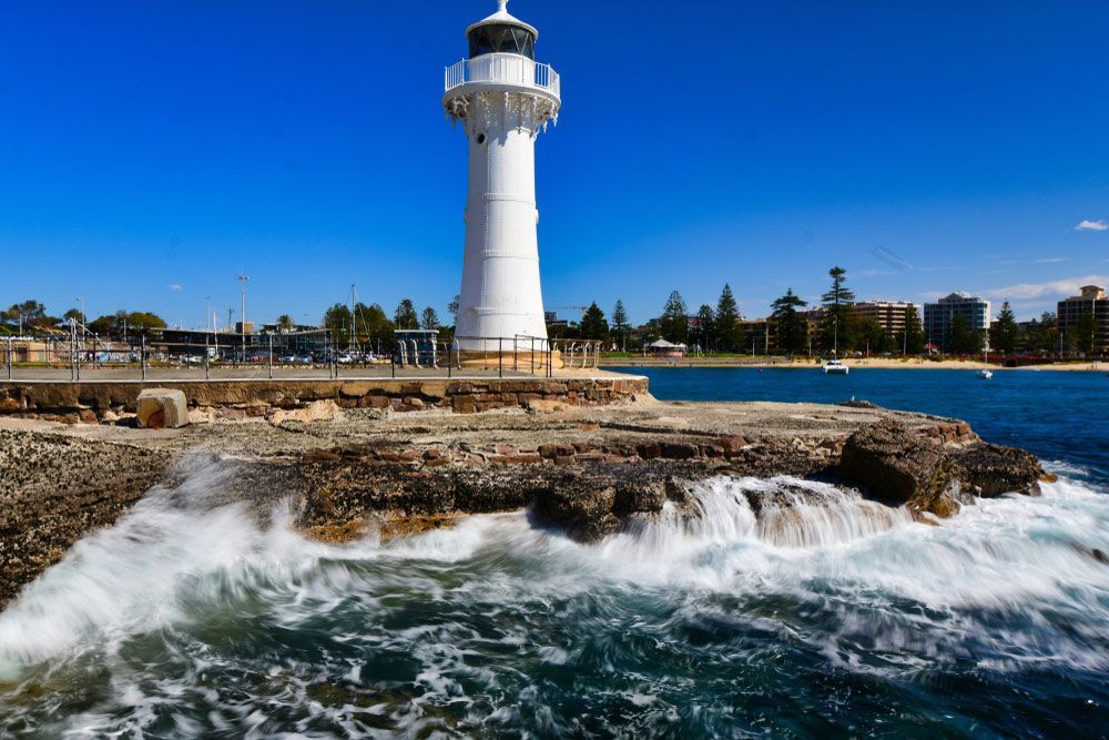 A Lighthouse Is Sitting On Top Of A Rocky Cliff Overlooking The Ocean — B Smart Building & Design In Wollongong, NSW