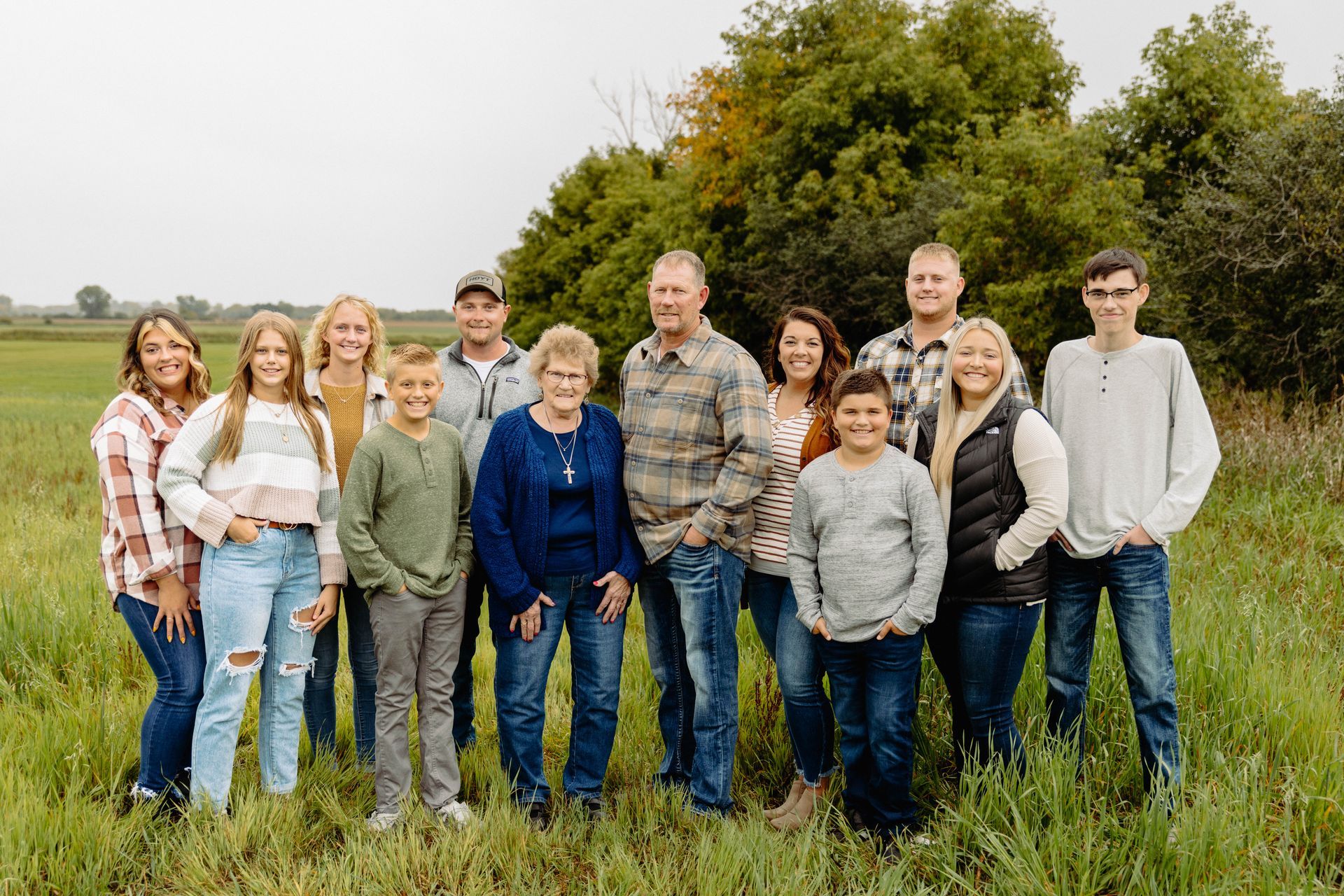 Family poses in a grassy field, smiling.  Adults and children in casual clothing; some looking at camera.