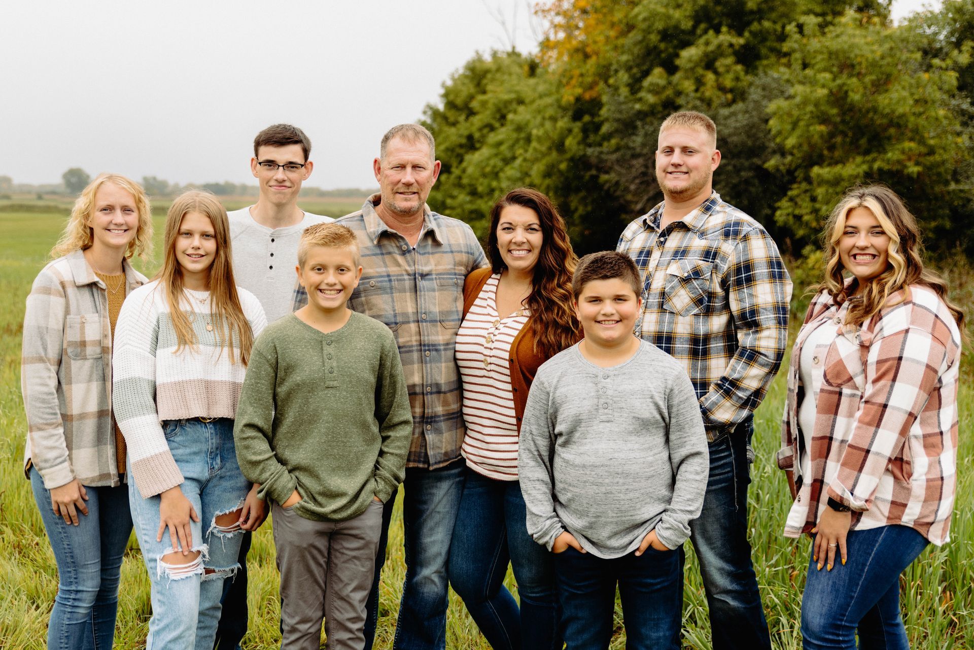 Family of eleven smiling, posed outdoors, in a field with trees in the background.