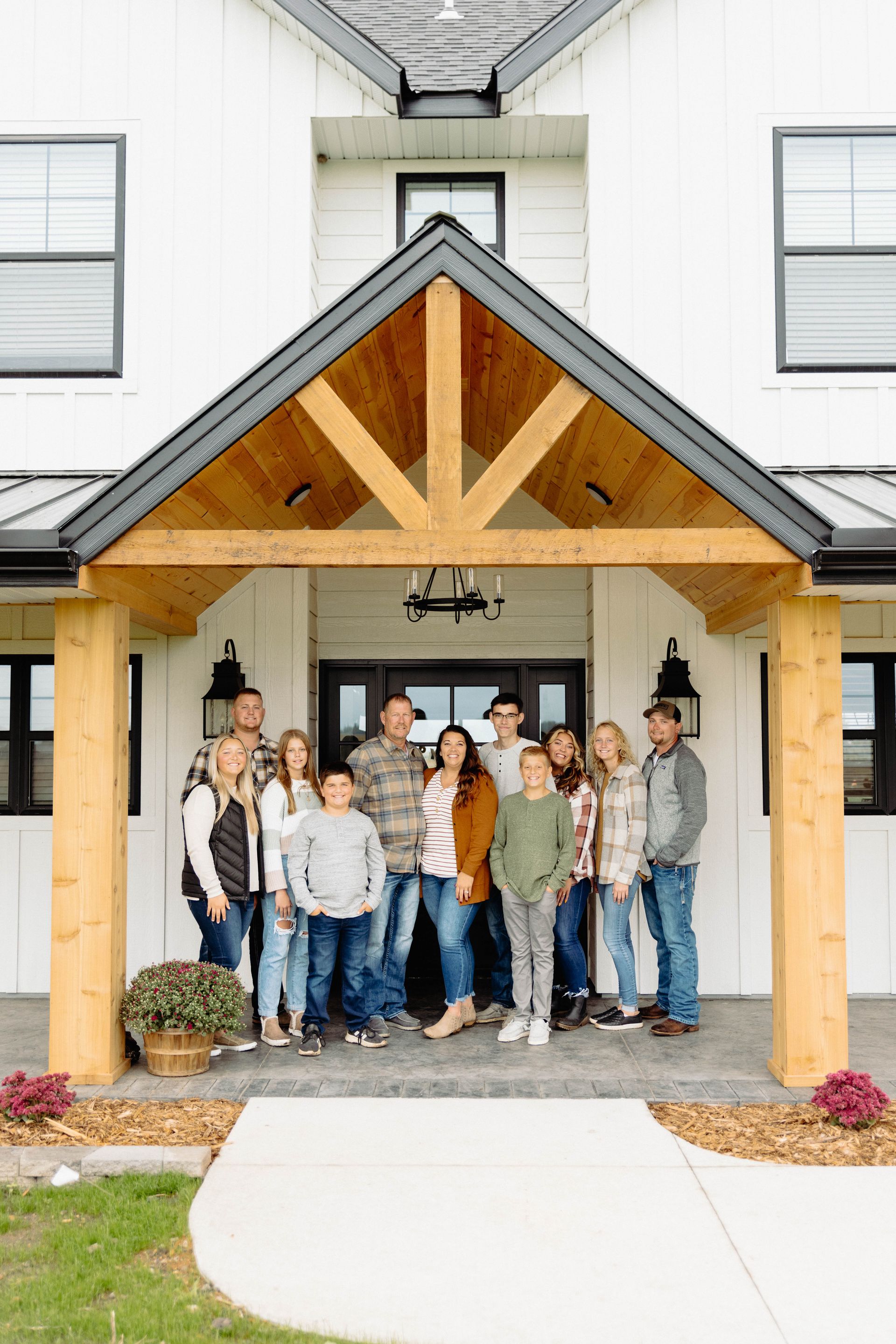 Family posing in front of a white farmhouse with a wooden porch.