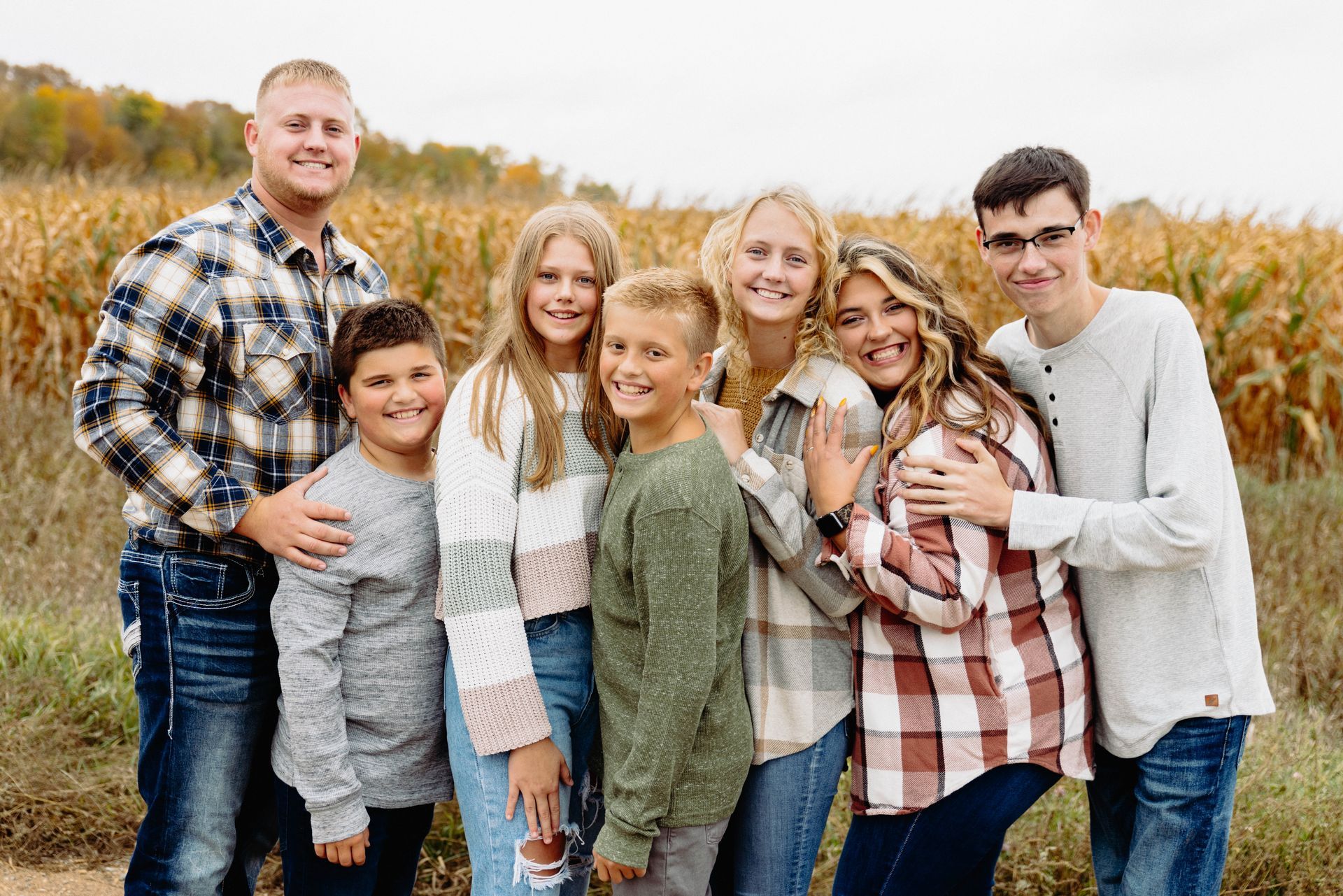 Family of seven smiling and posing in front of a cornfield; Fall colors.