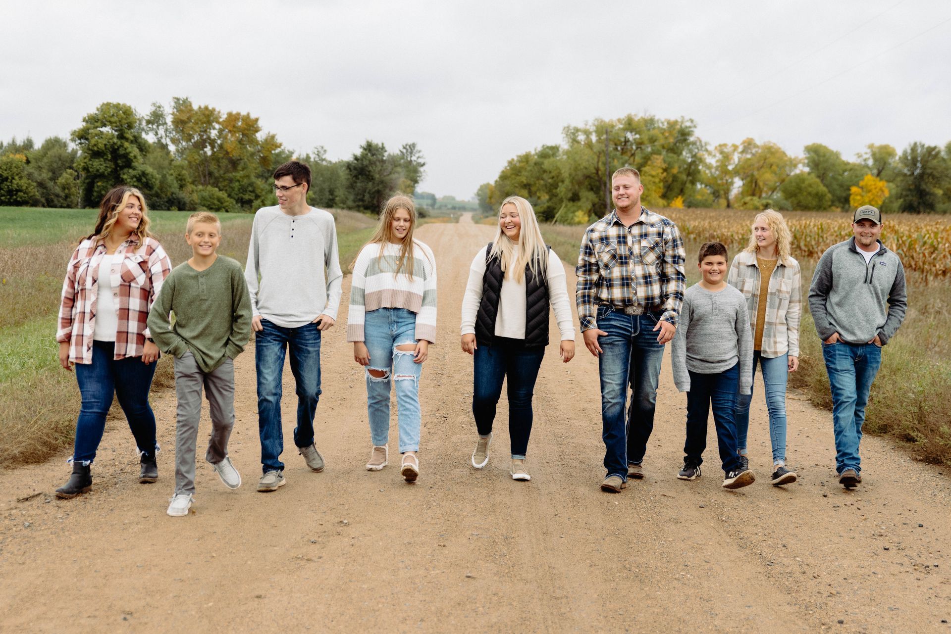 Family of ten walking down a dirt path, smiling, in a rural setting.