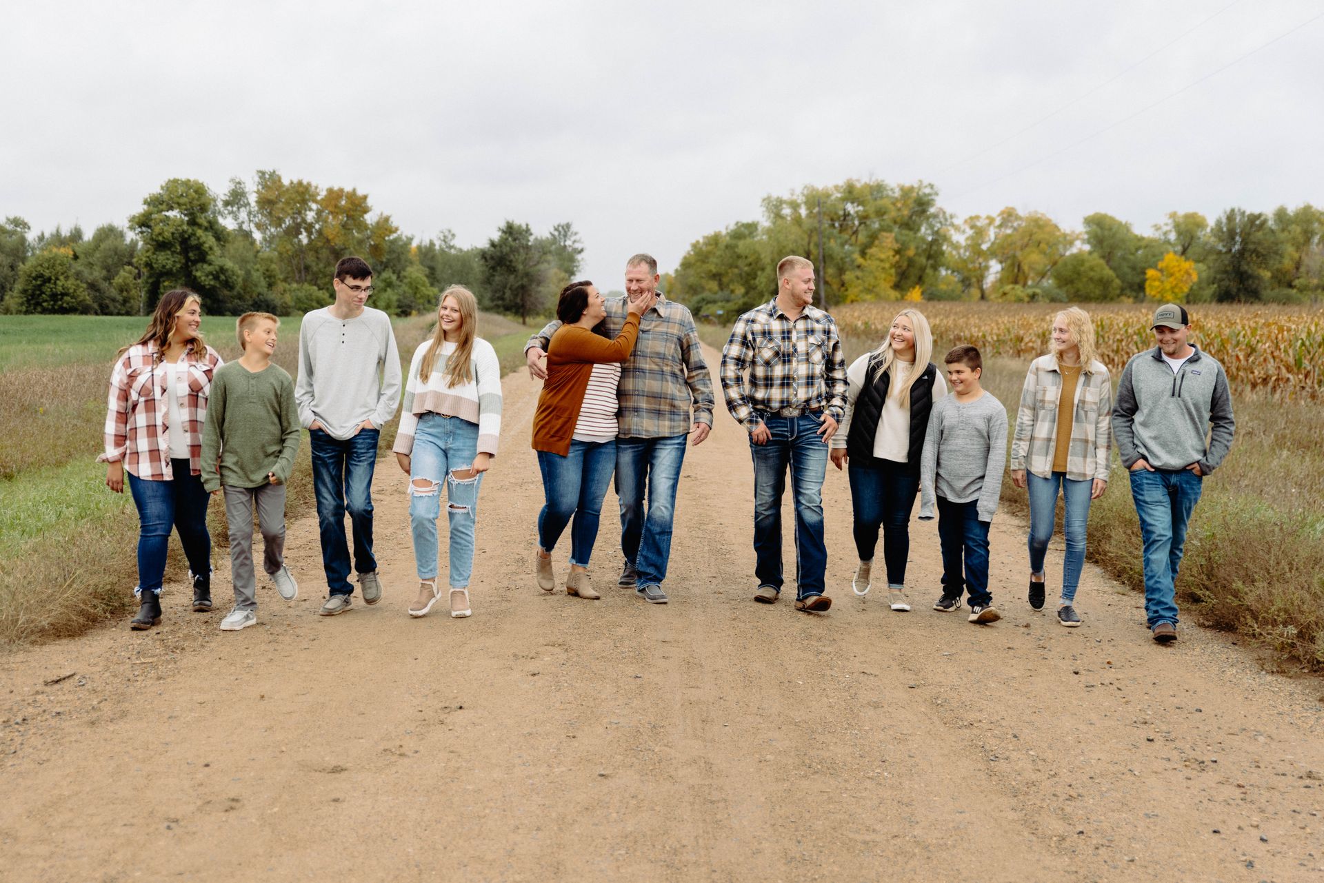 Family of 11 walking down a dirt road in a field. Autumn setting; various expressions and clothing styles.