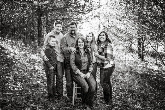 Family of six poses in a wooded area, smiling. Black and white photo. Family photo taken in Minnesota.