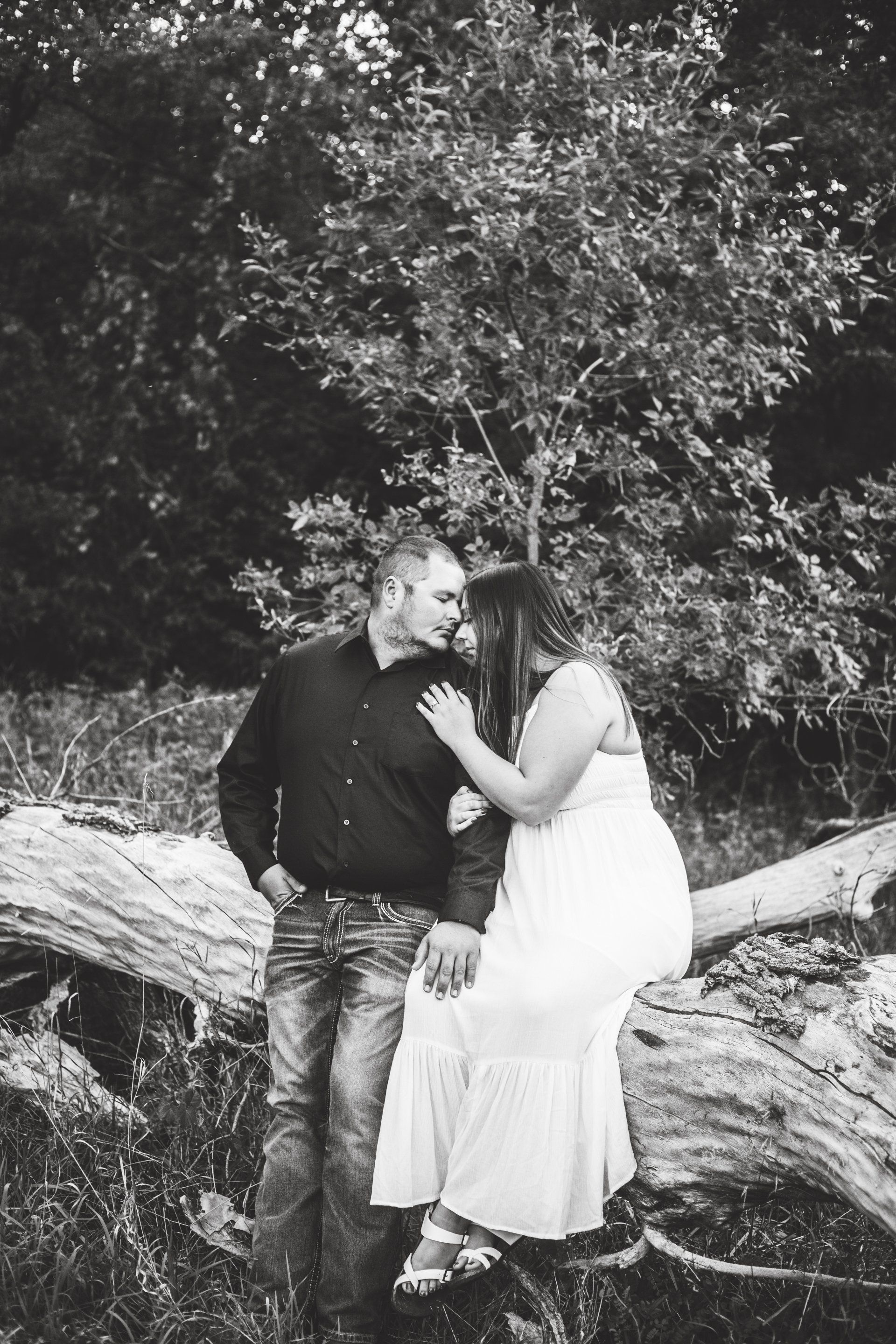 Couple embracing on a fallen tree in a wooded area; black and white photo.
