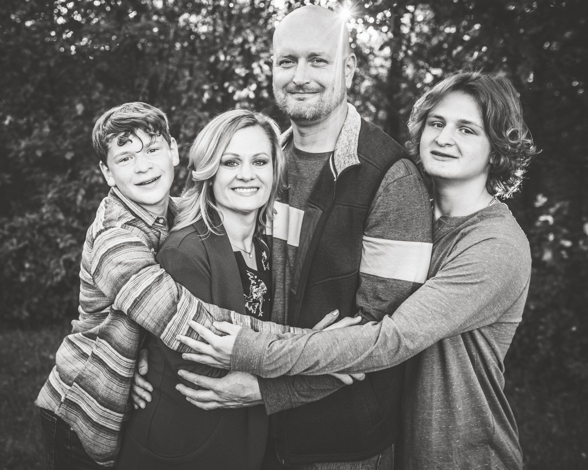Family of four smiling and embracing outdoors in black and white.