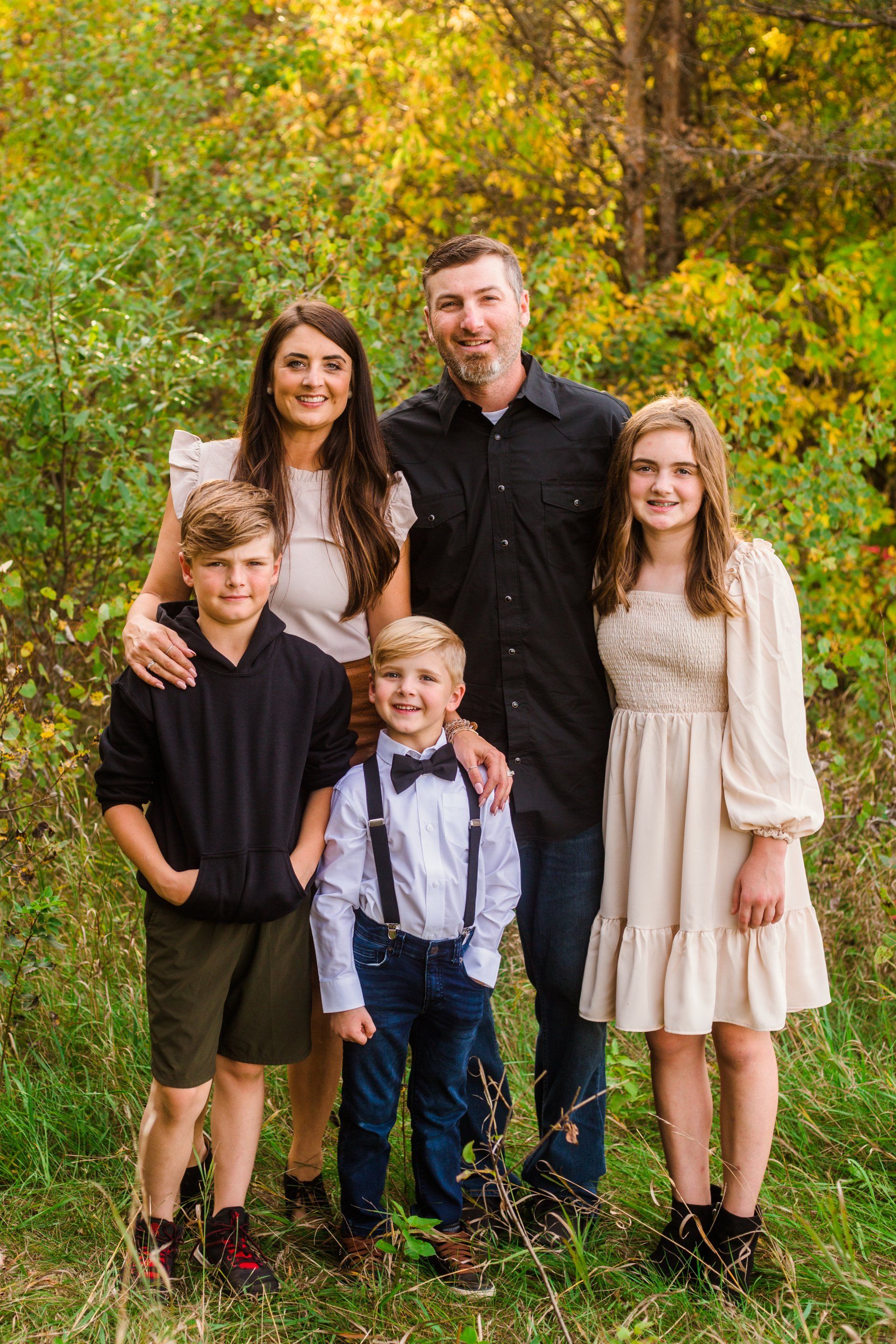 Family of five poses outdoors; fall foliage in background.