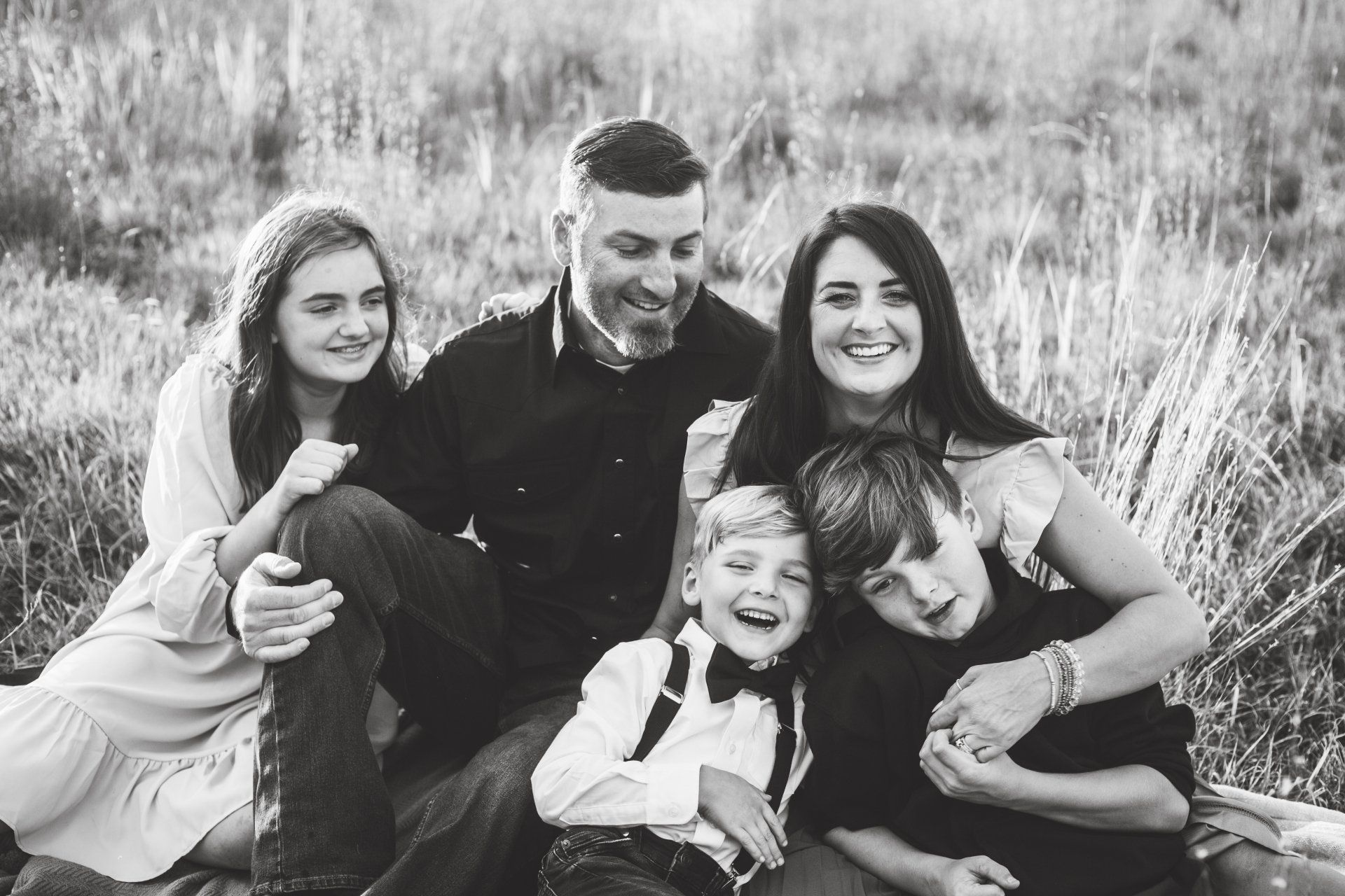 Family of five smiling in a field. Parents and three children pose closely together.
