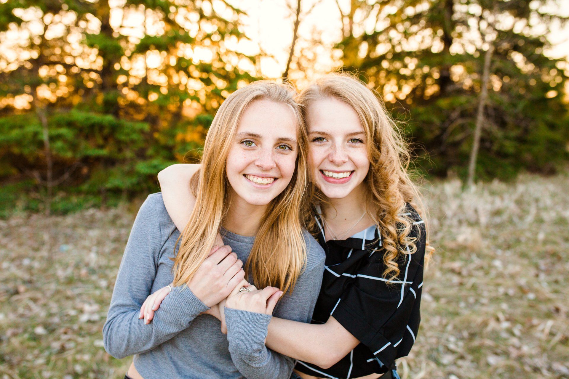 Two blonde women in the fall outdoors and hugging each other, getting their picture taken.