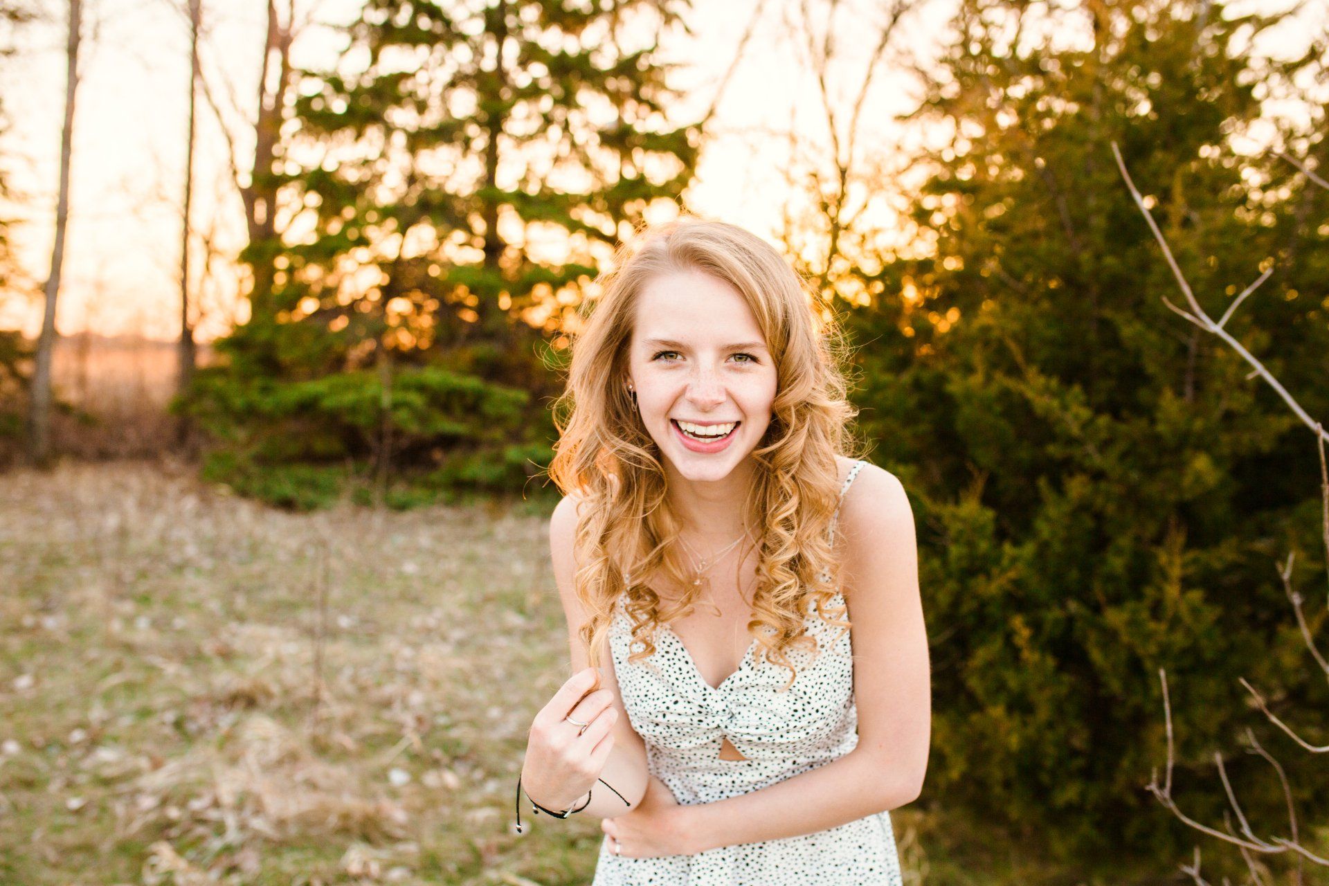 Woman laughing with curly blonde hair, outdoors at sunset.