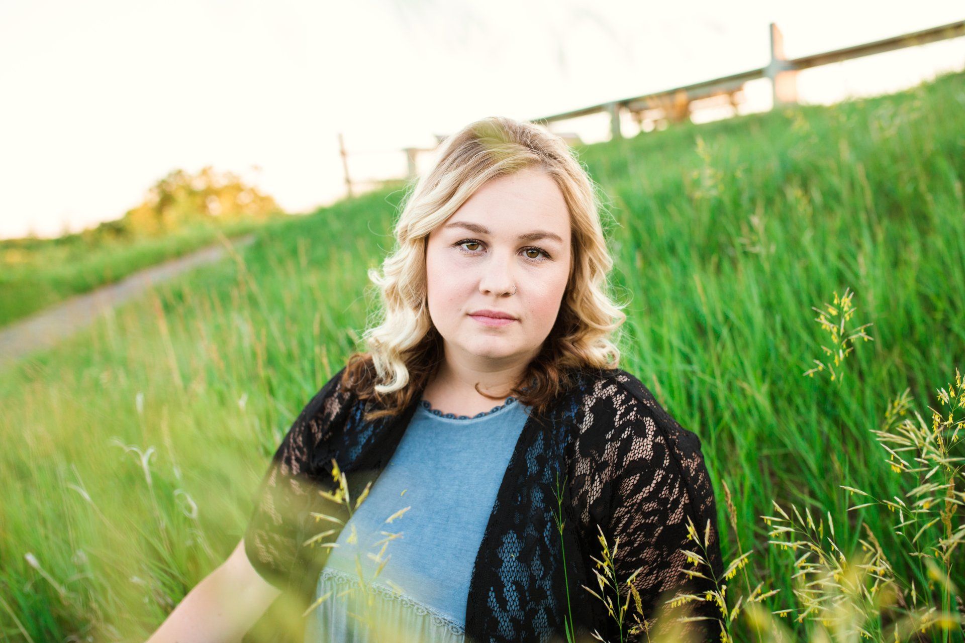 Blonde woman in blue dress and black lace shawl, in tall green grass.