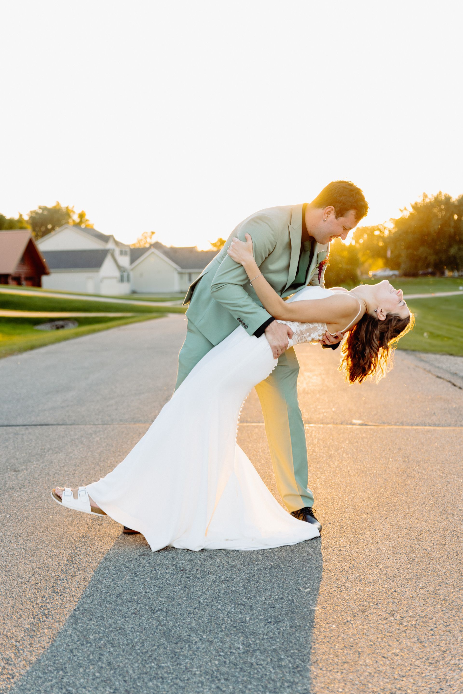 Bride and groom dancing on a road at sunset; the groom dips the bride.