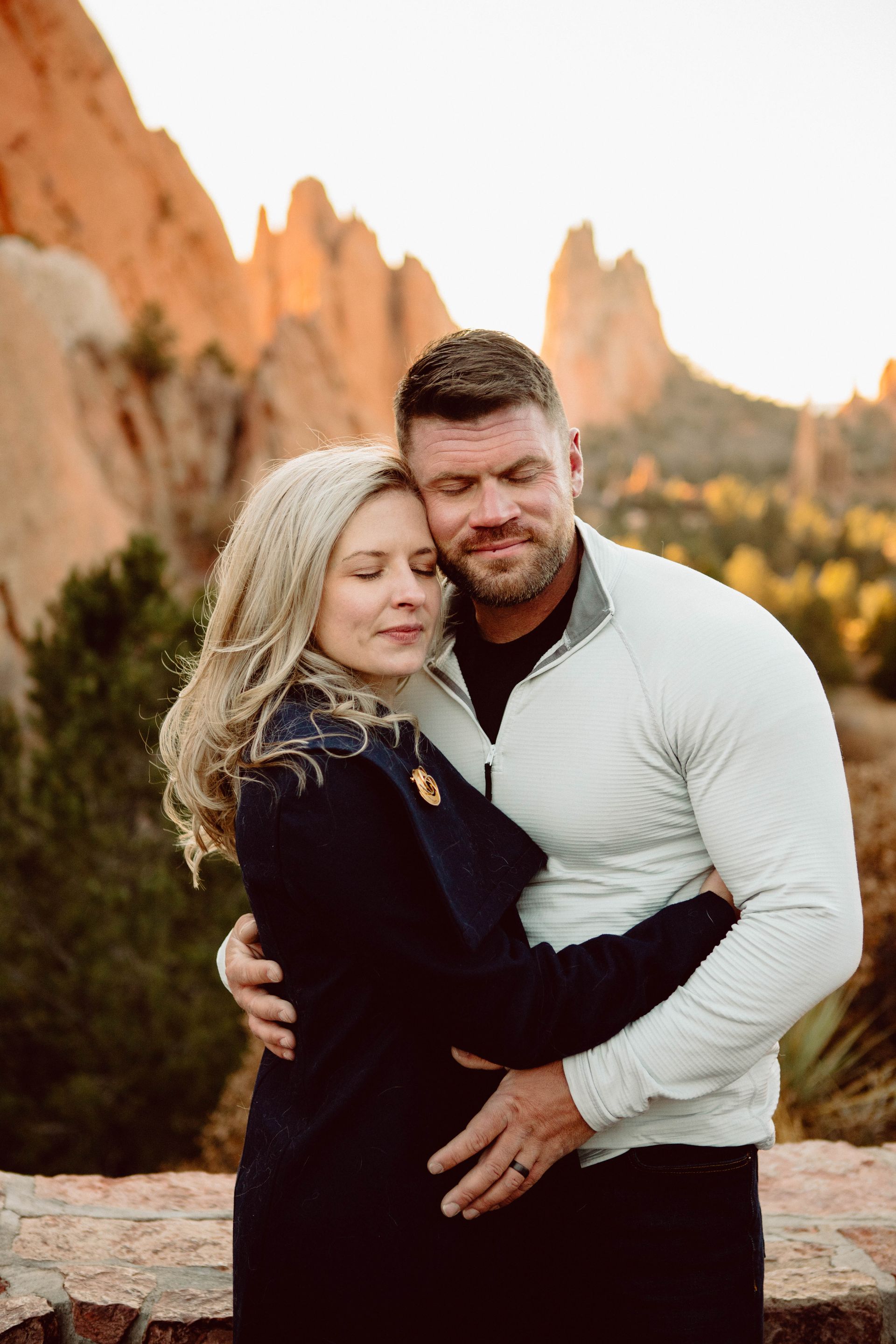 Couple embracing, eyes closed, at Garden of the Gods. Man's arm around woman. Sunset glow.