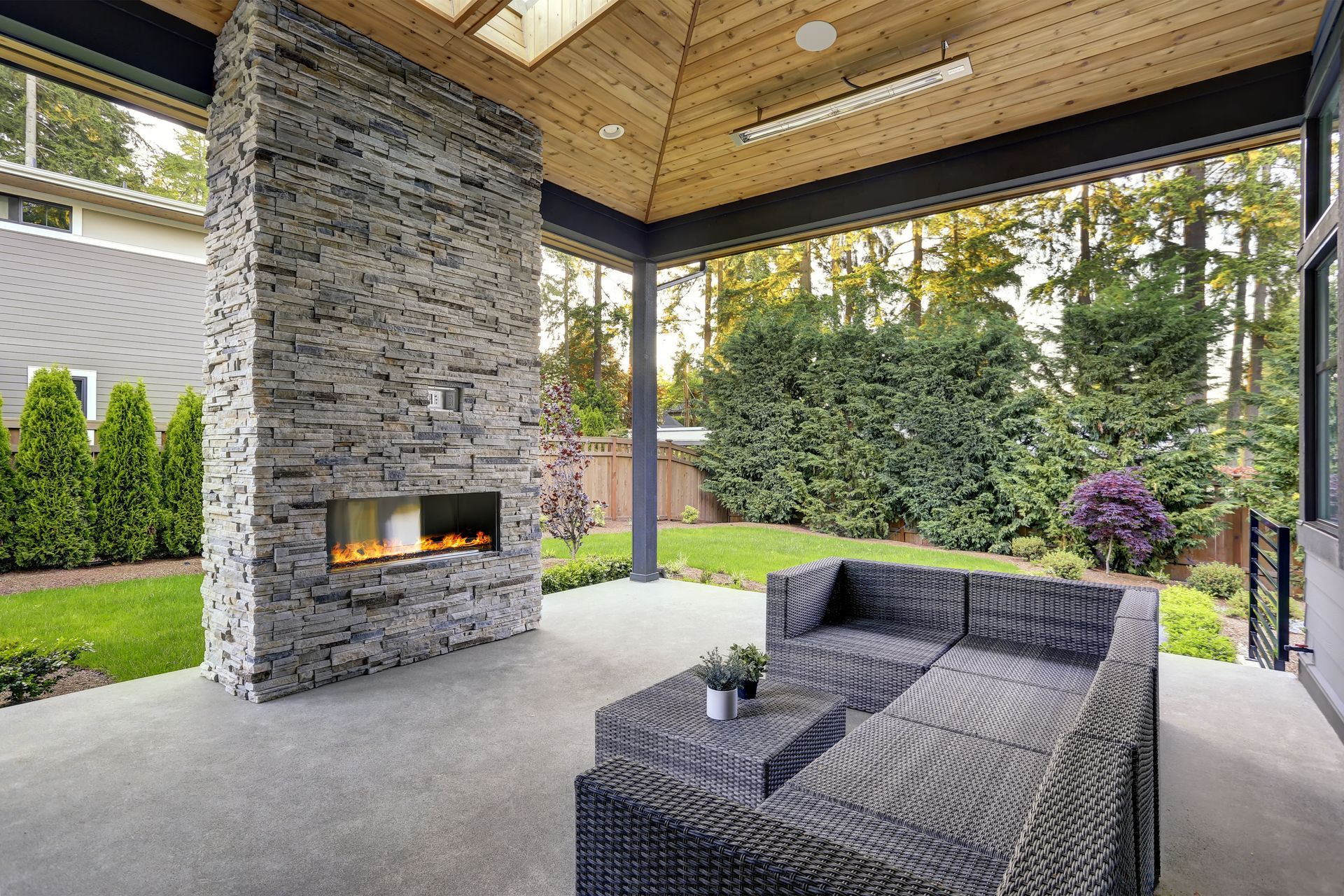 Covered patio with stacked stone fireplace, outdoor seating, and lush greenery.