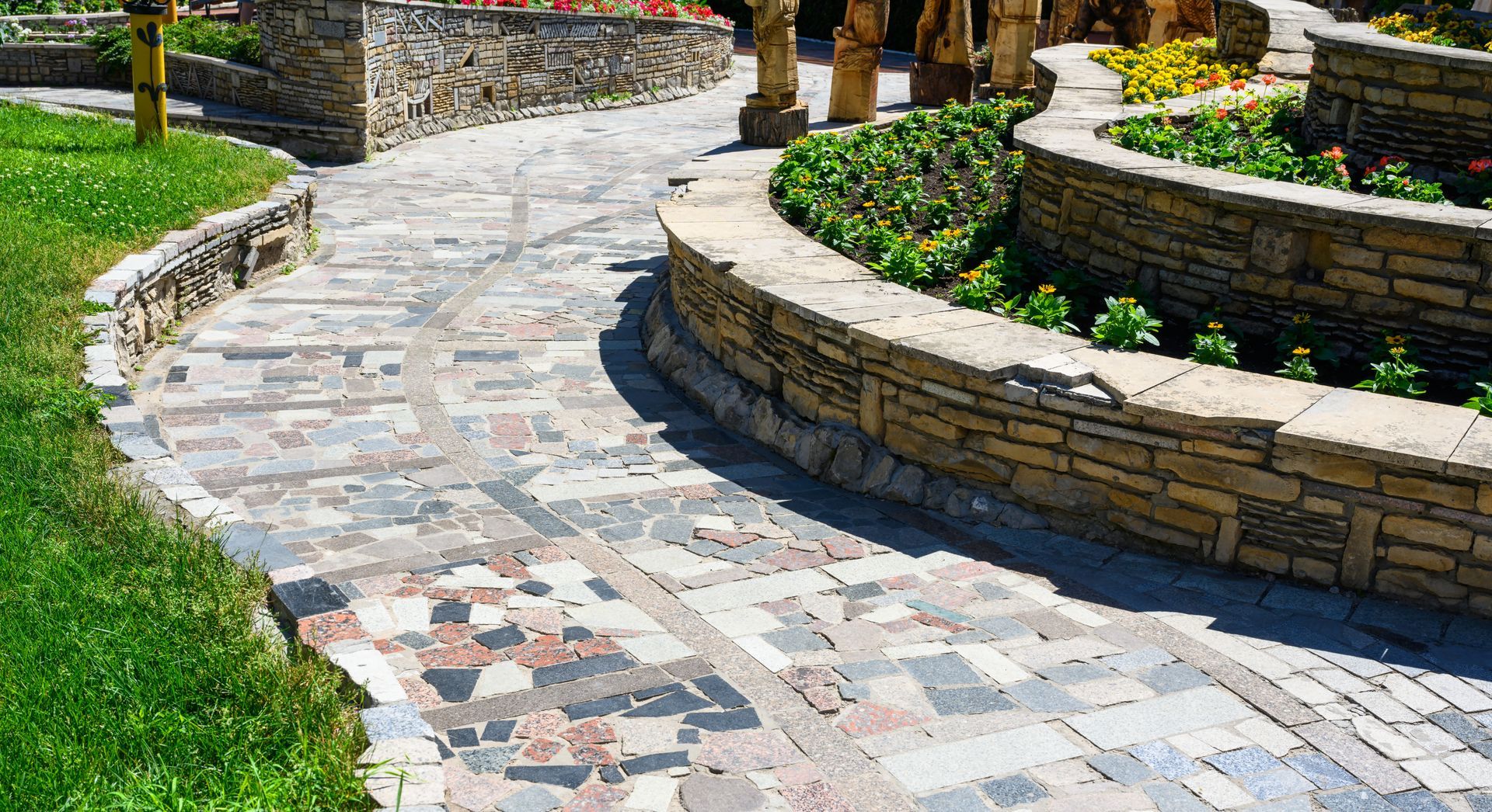 A stone walkway in a park surrounded by flowers and grass.