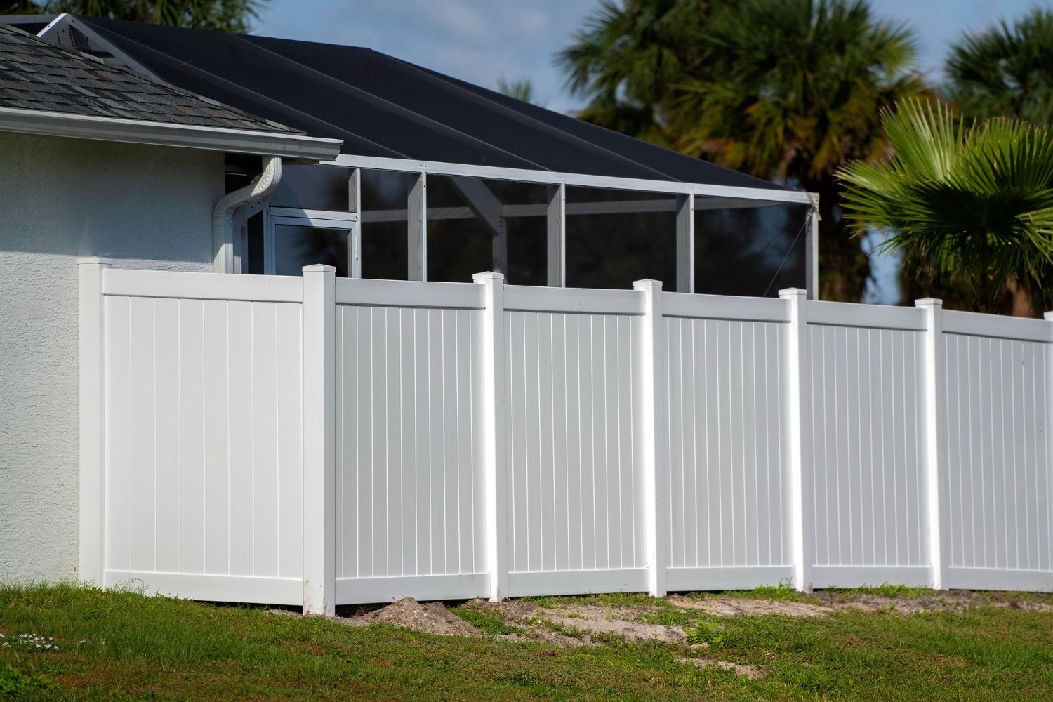 A white fence surrounds a house with a screened in porch.