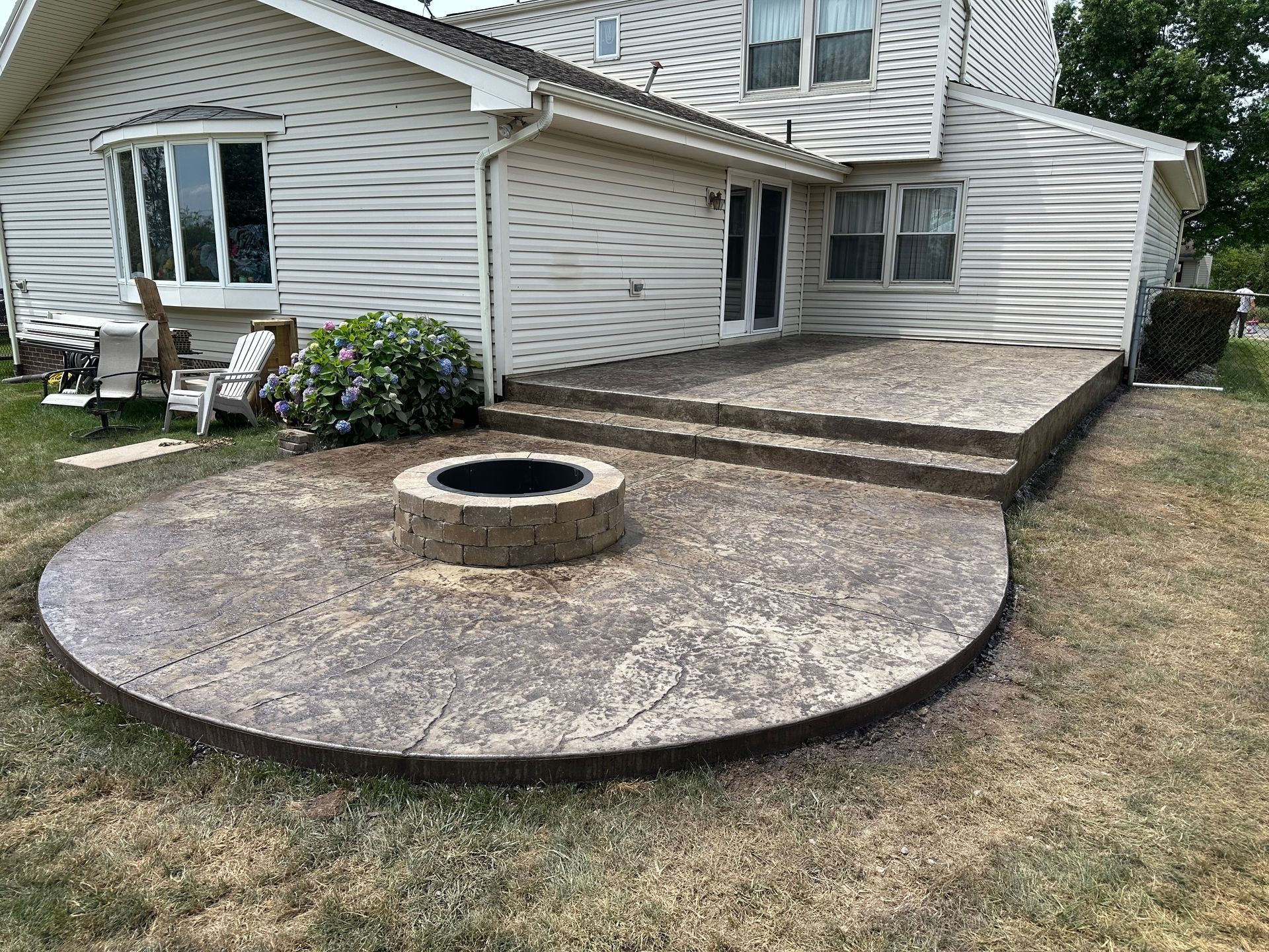 White house patio with a curved brick walkway and a circular fire pit in the foreground