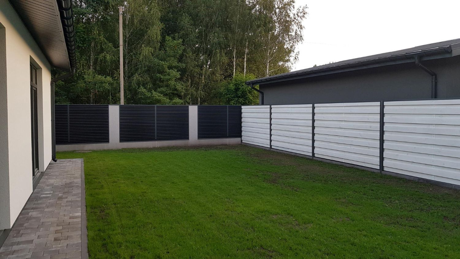 A white fence surrounds a lush green lawn in front of a house.