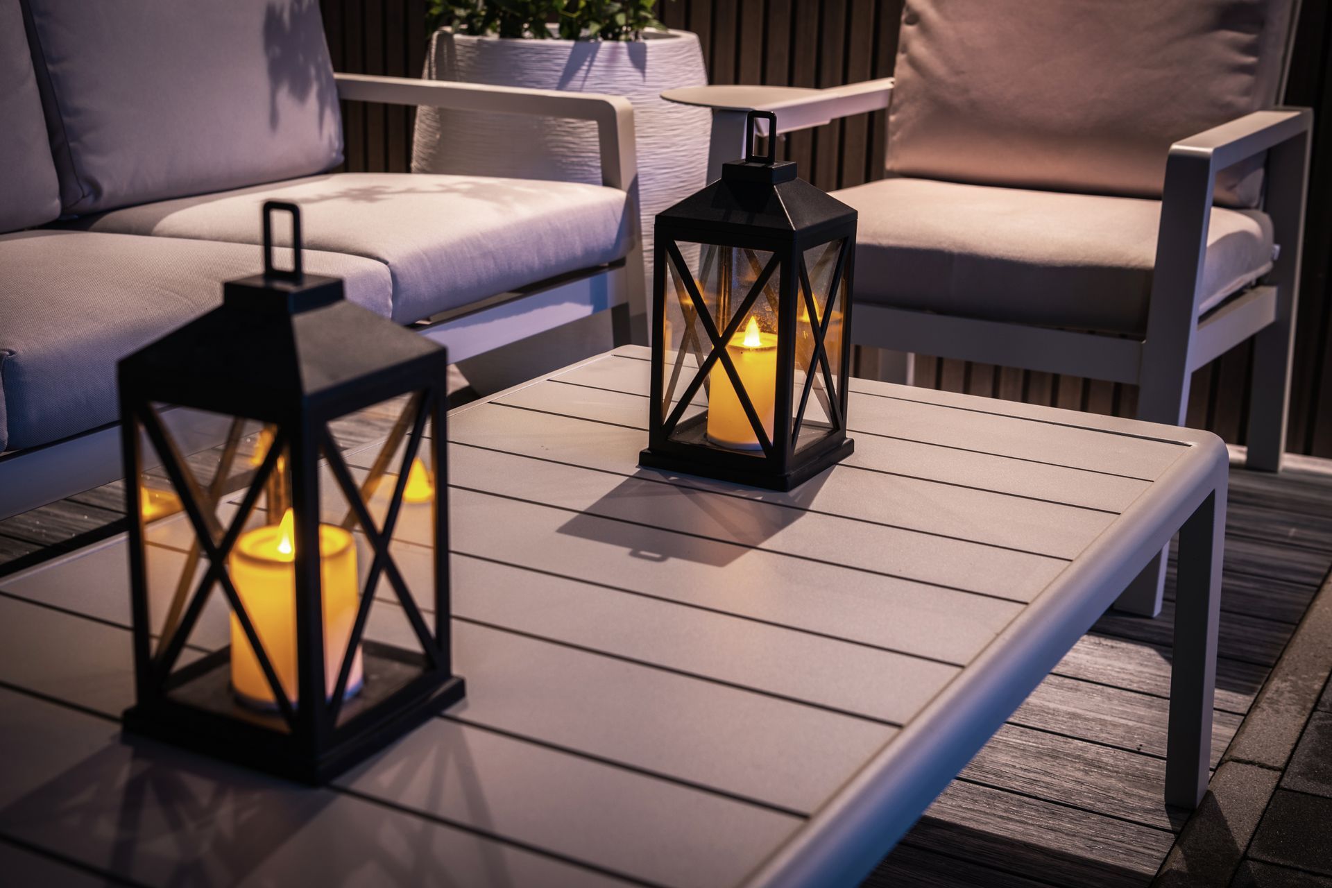 Two lit black lanterns on a grey table; patio seating in background.