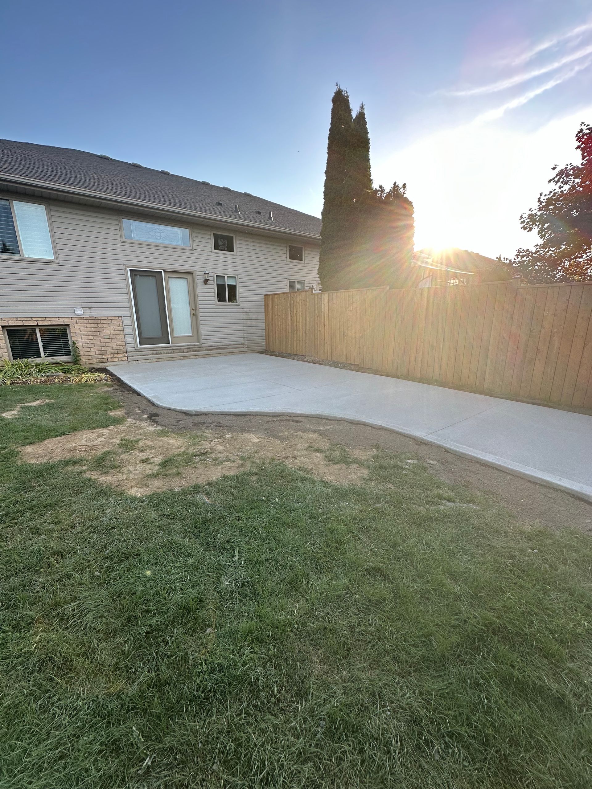 A man in a blue shirt is working on a concrete walkway in front of a brick house.