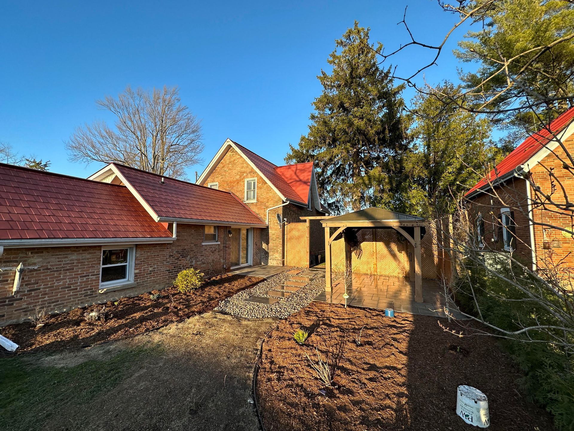 Brick house with red roof, landscaped yard, and wooden arbor on a sunny day.