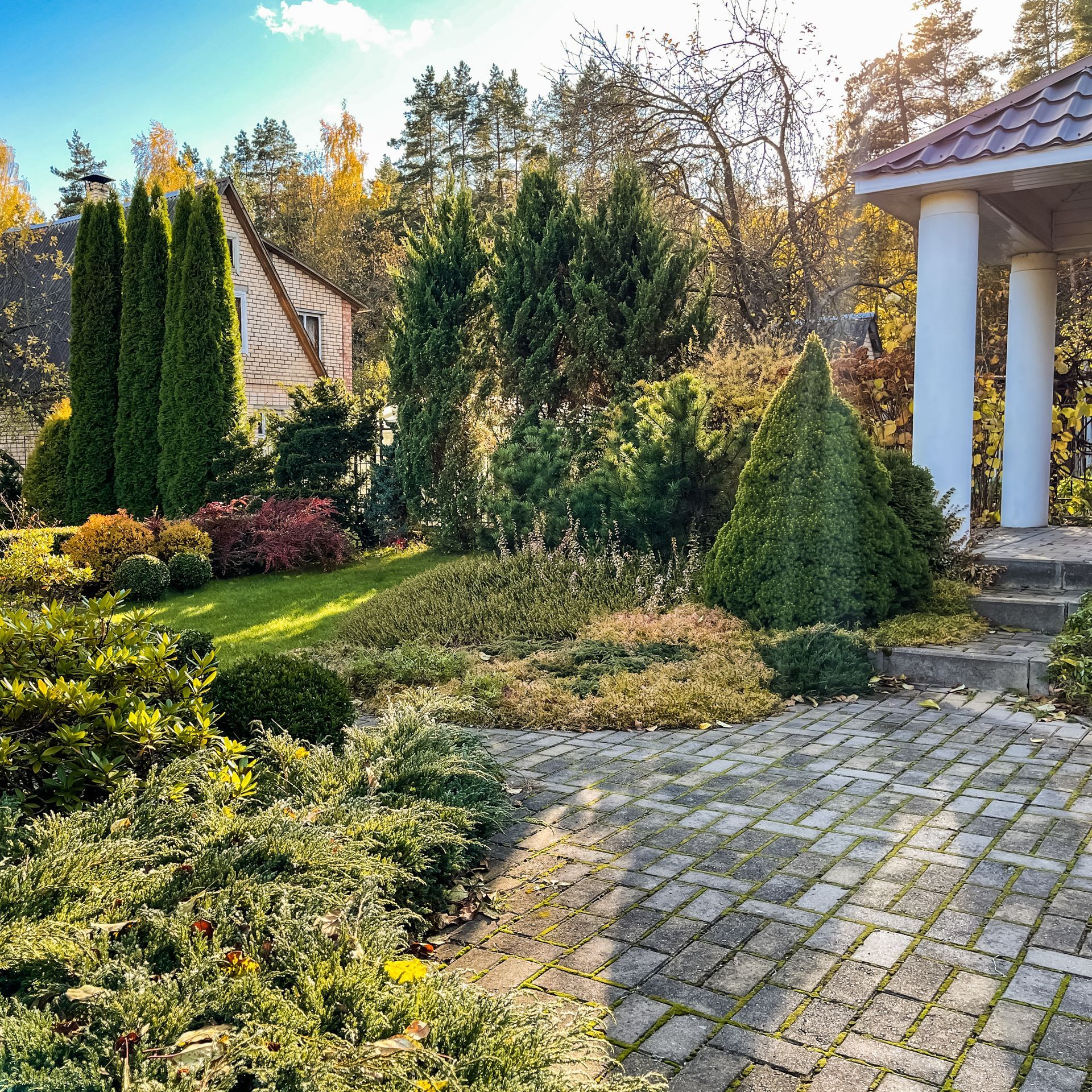 A brick walkway leads to a gazebo in a garden surrounded by trees and bushes.