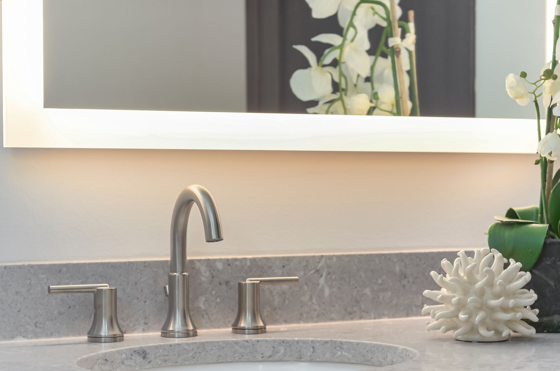 Modern bathroom sink with silver faucet, lit mirror, and decorative coral.