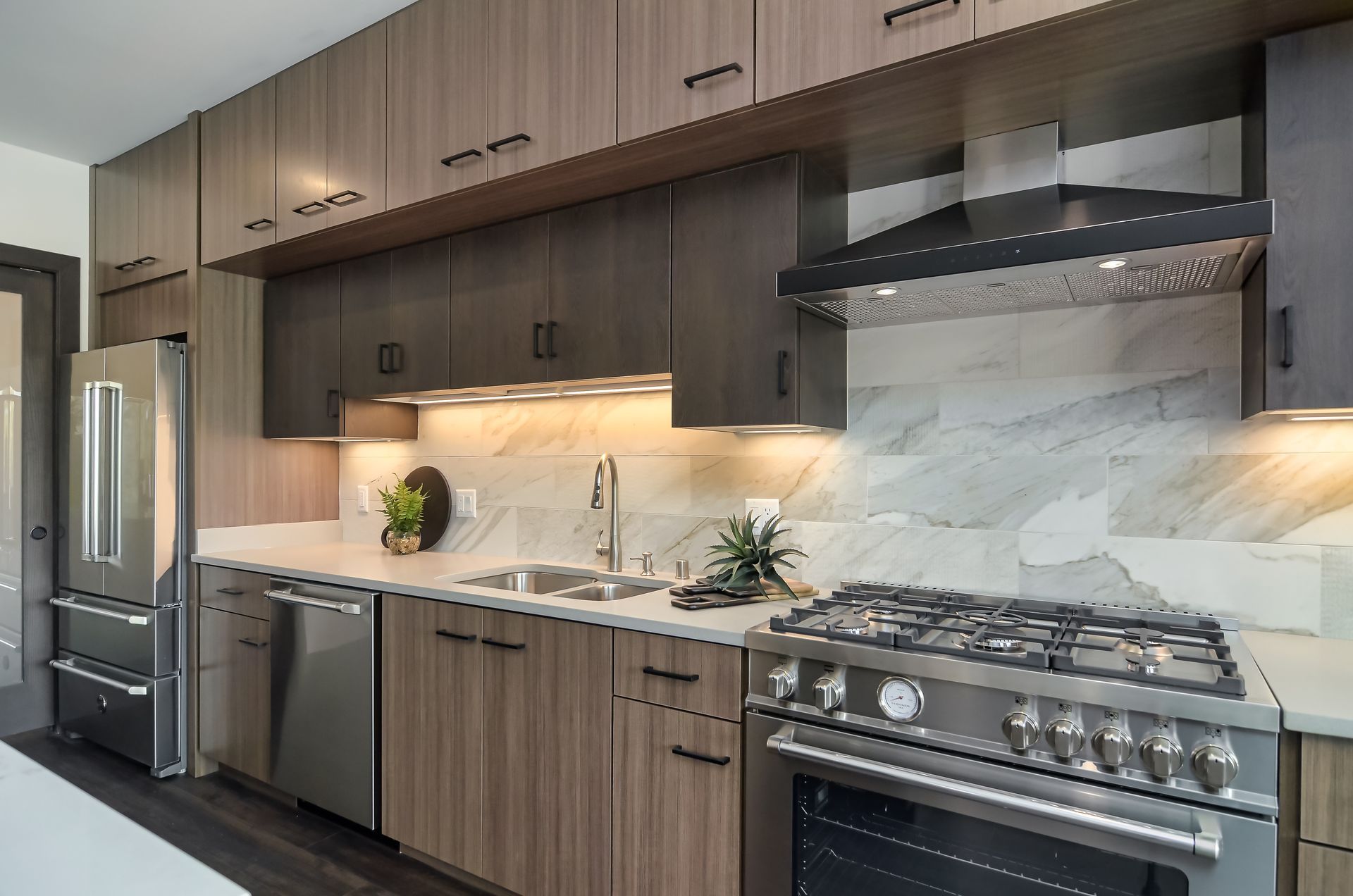Modern kitchen with stainless steel appliances, dark wood cabinets, and marble backsplash.