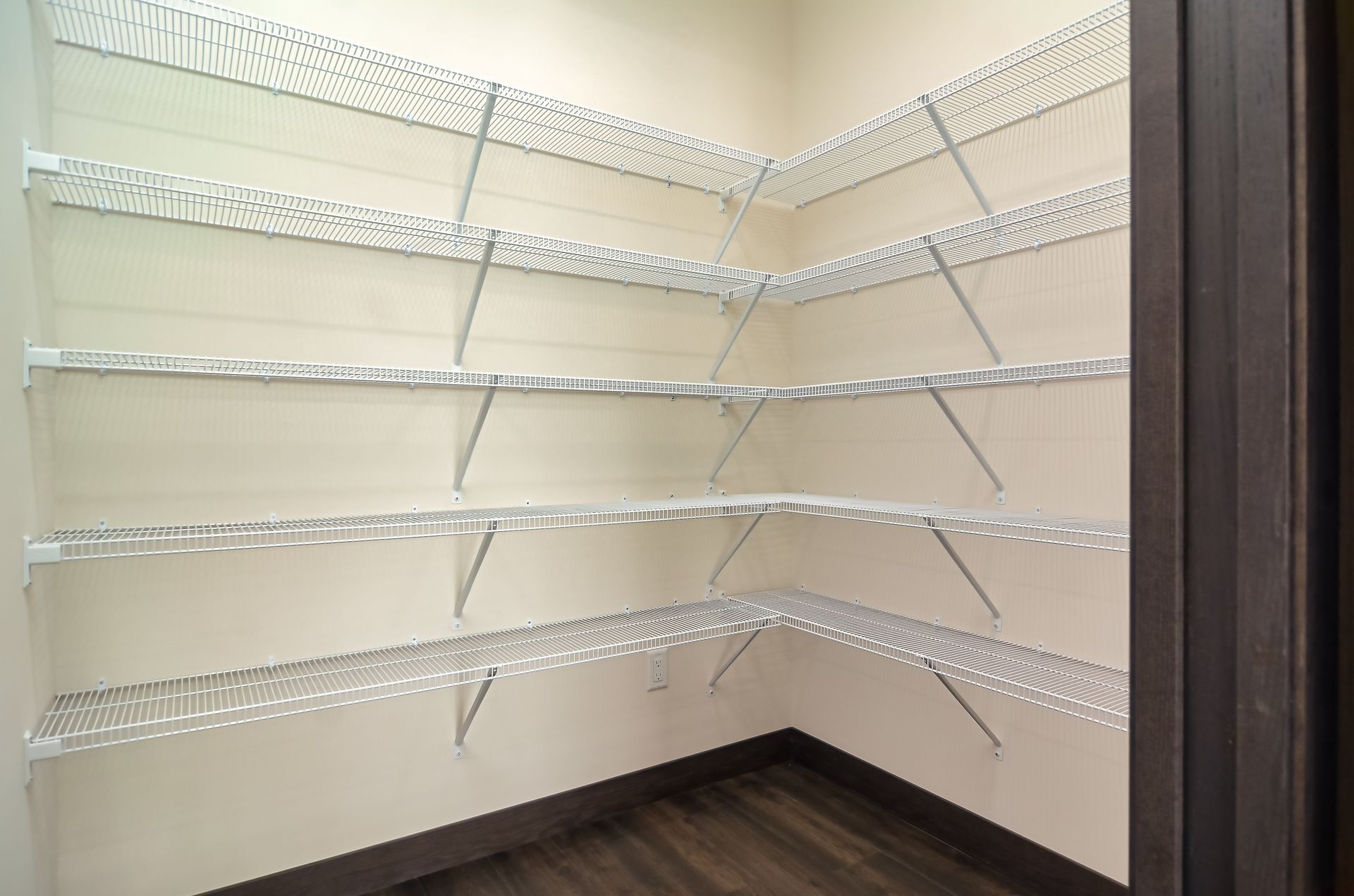 Empty pantry with wire shelving in a corner. Light walls and dark floor.