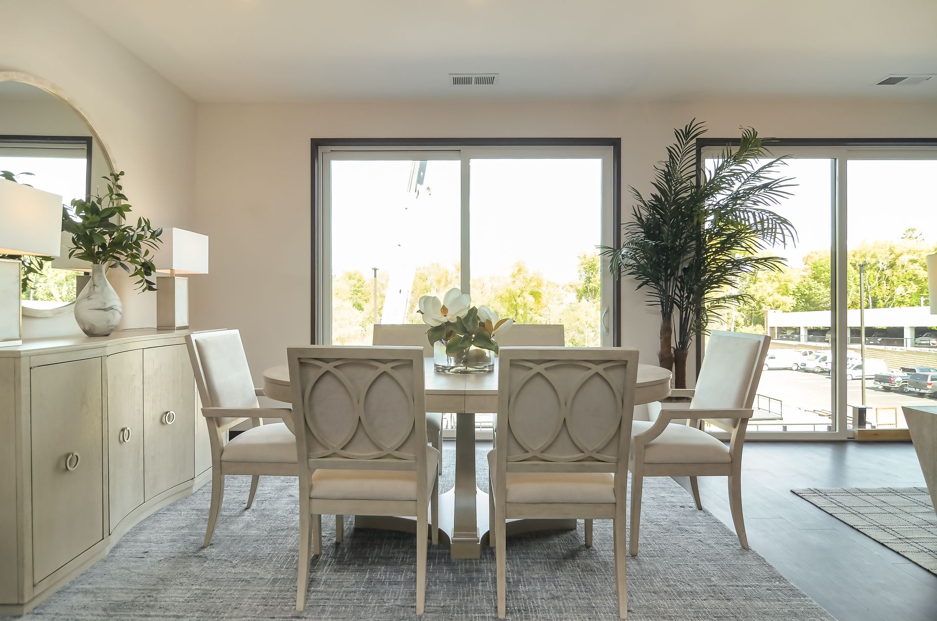Dining room with a table, chairs, buffet, mirror, and large window overlooking trees.