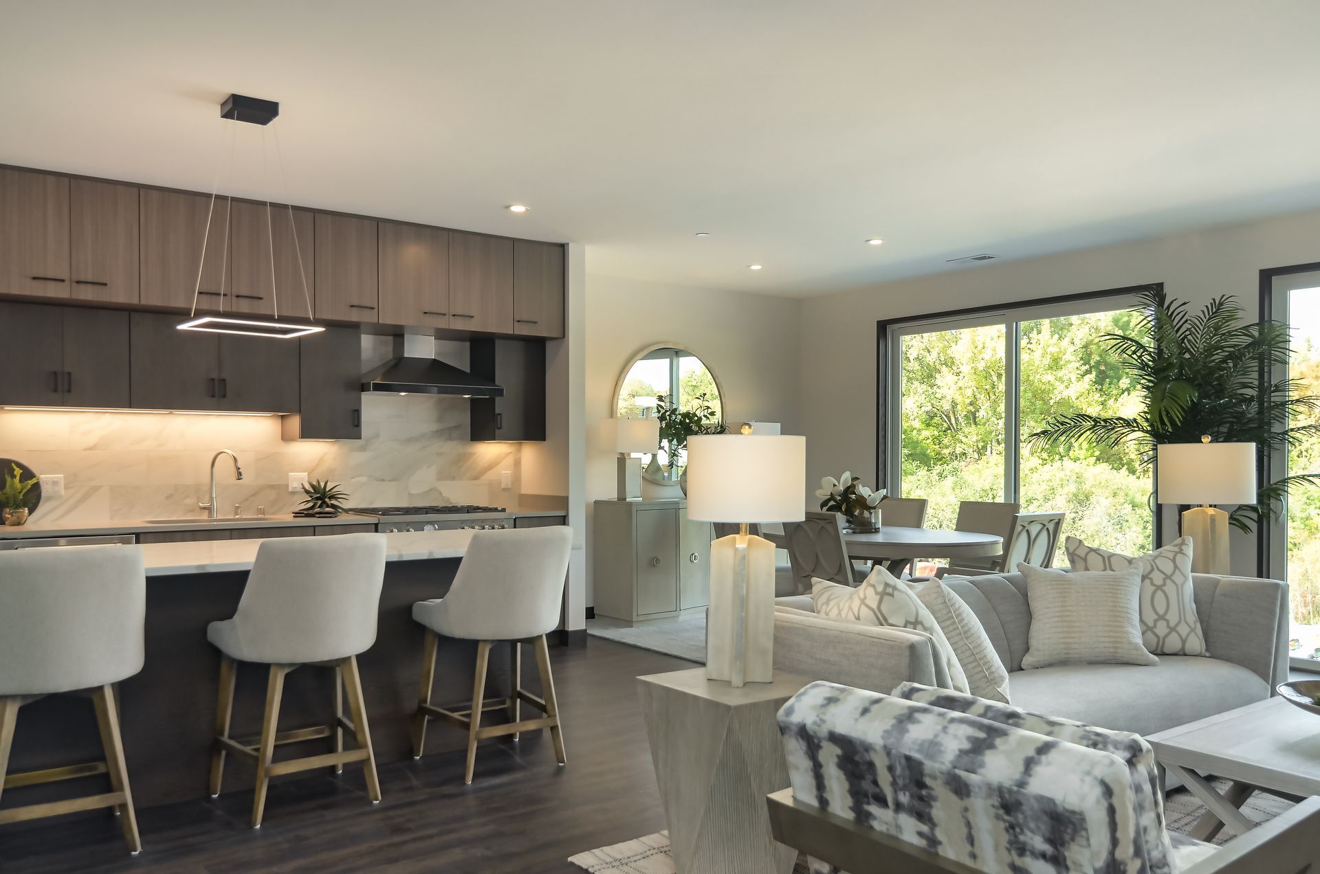 Modern open-concept living space with kitchen island, living room, and dining area overlooking a sunny exterior.