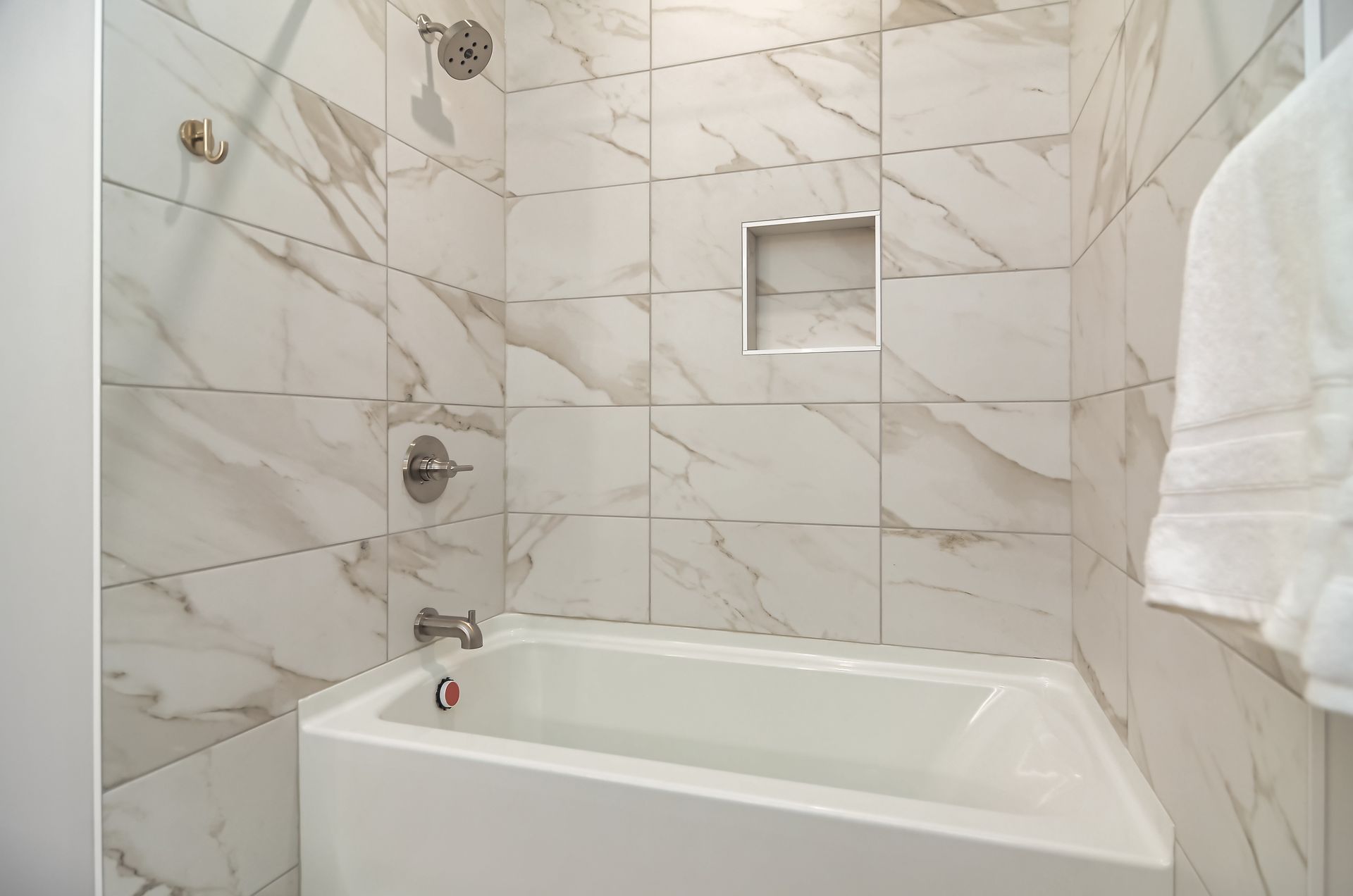 White tiled bathroom with a bathtub, showerhead, and a towel hanging on the right.