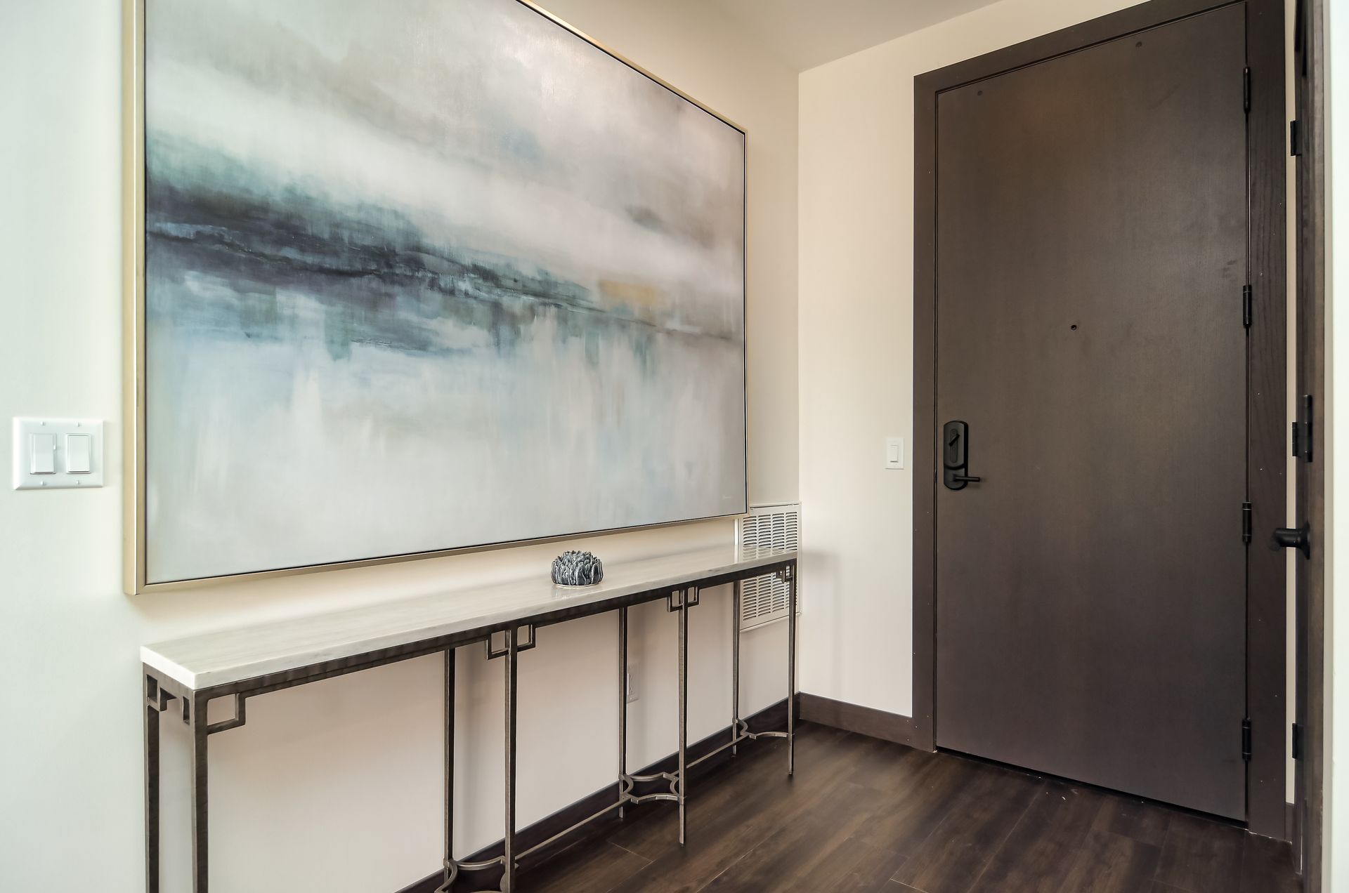 Entryway with abstract painting above a console table and a dark brown door.