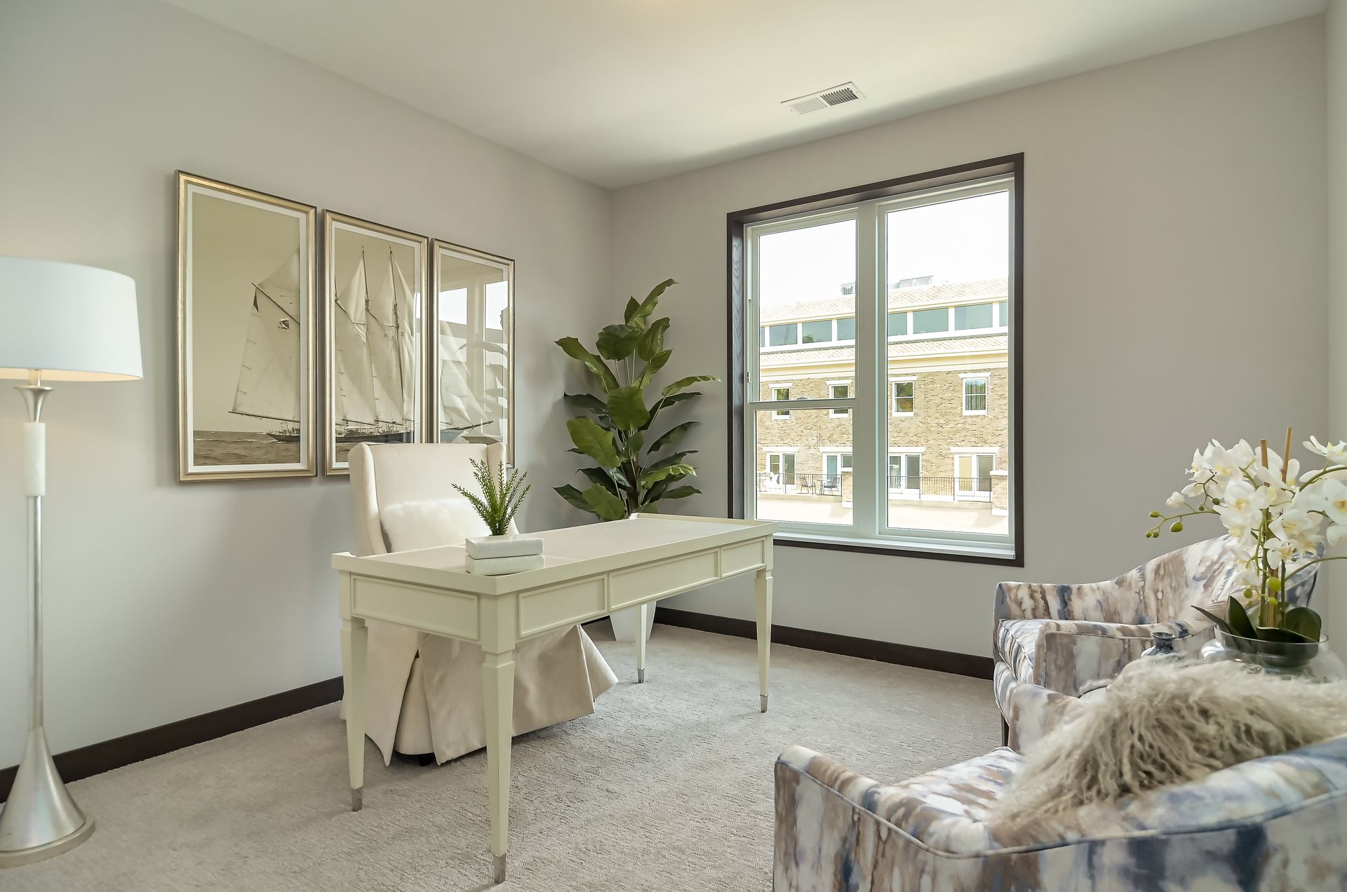 Office with desk, armchair, floor lamp, mirrors, and large window; neutral colors.