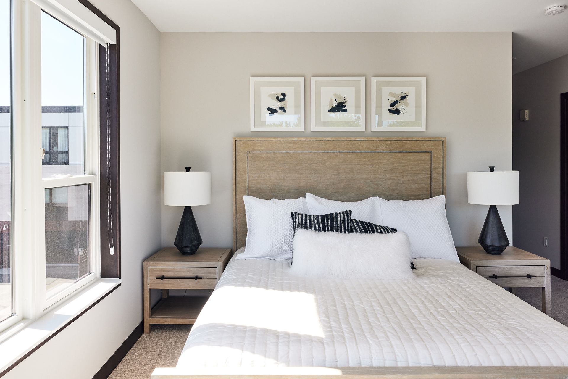 Bedroom with bed, nightstands, lamps, artwork, and large window. Neutral color scheme.