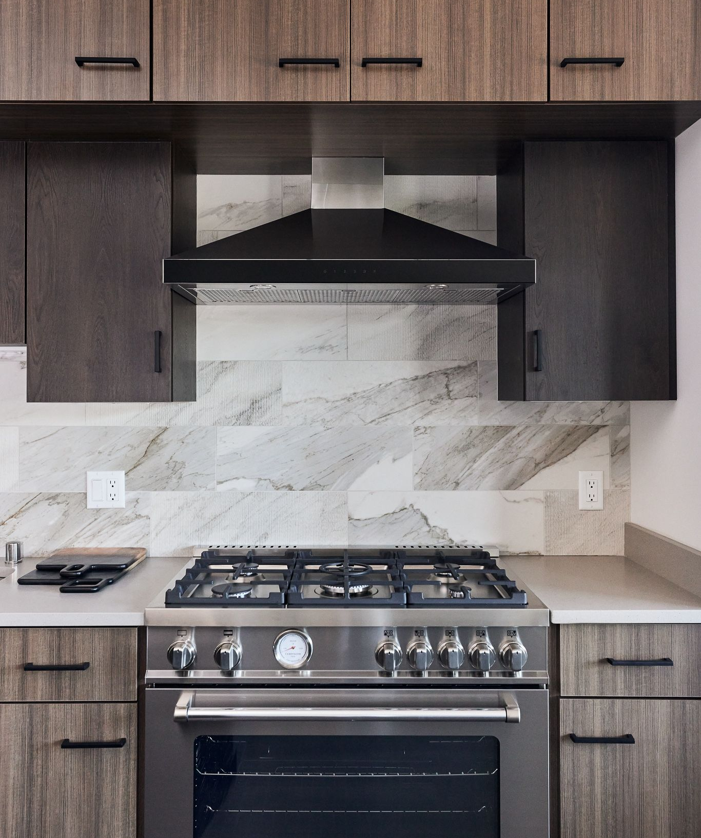 Modern kitchen with stainless steel stove, dark cabinets, marble backsplash, and range hood.