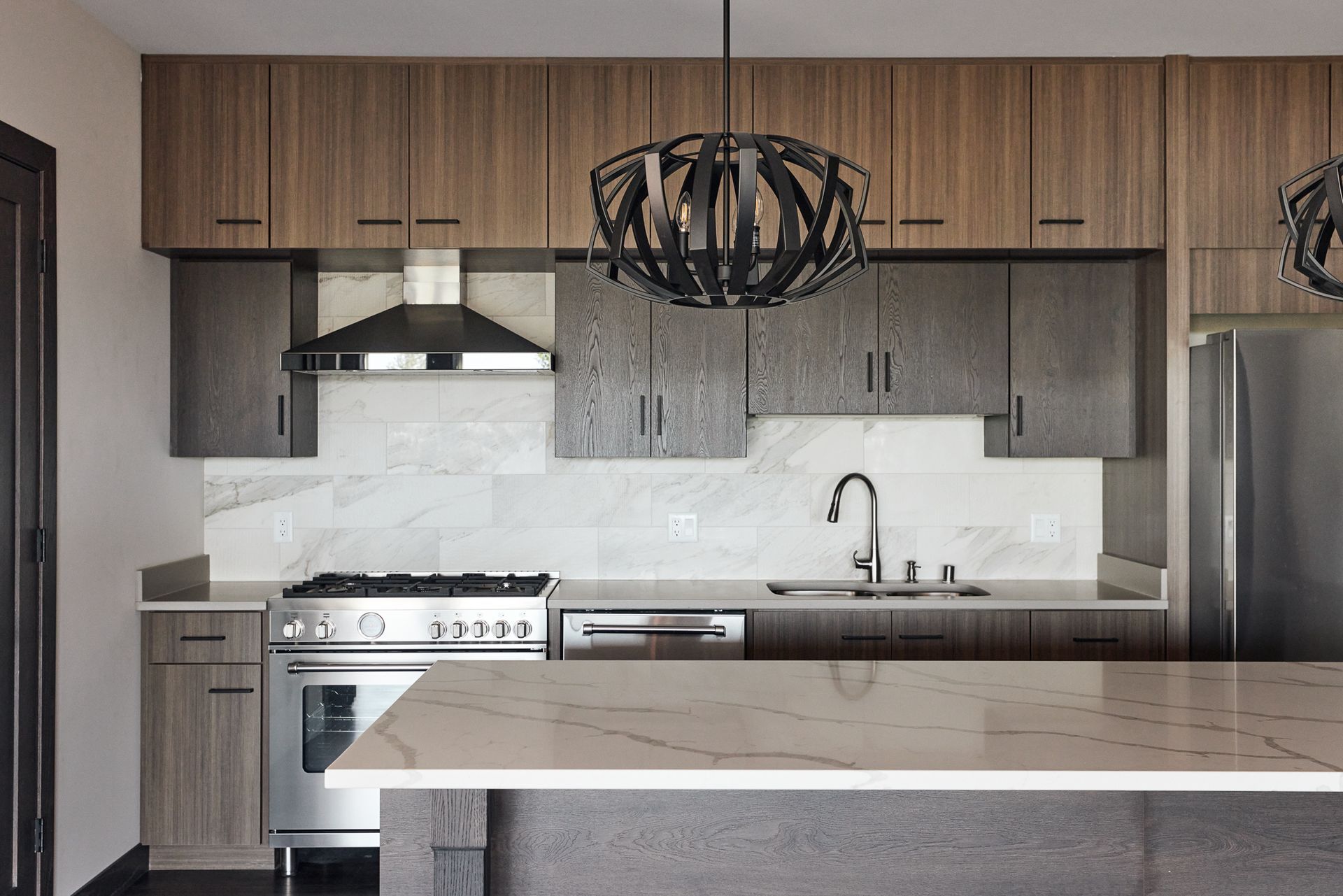 Modern kitchen with wood and gray cabinets, stainless steel appliances, and a marble countertop.