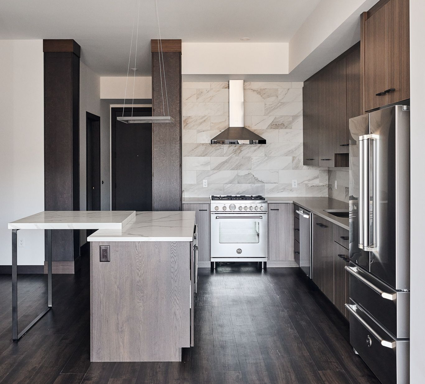 Modern kitchen with wood cabinets, stainless steel appliances, marble island, and dark wood floor.